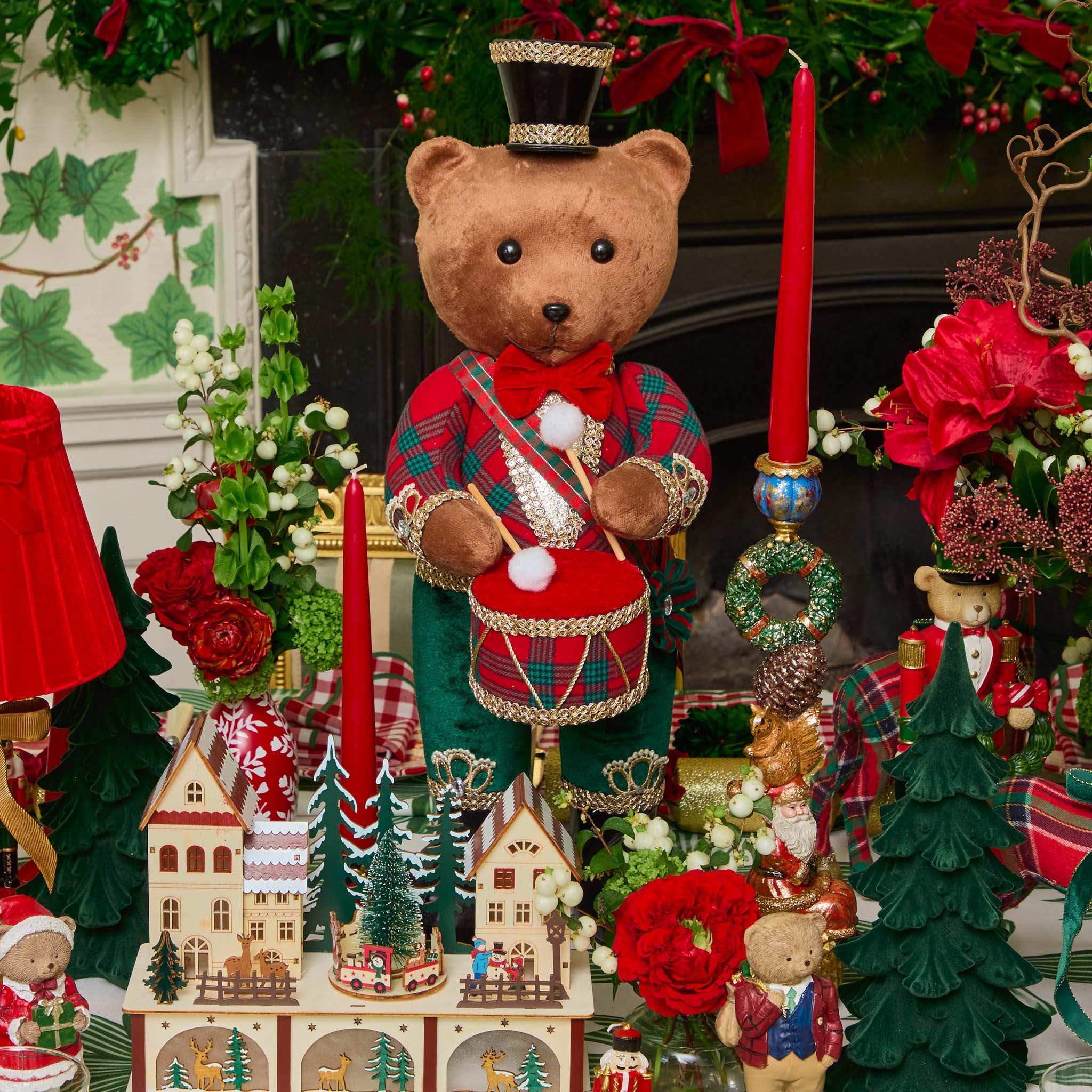 Decorative scene with a teddy bear in a festive outfit, candles, and Christmas decorations.