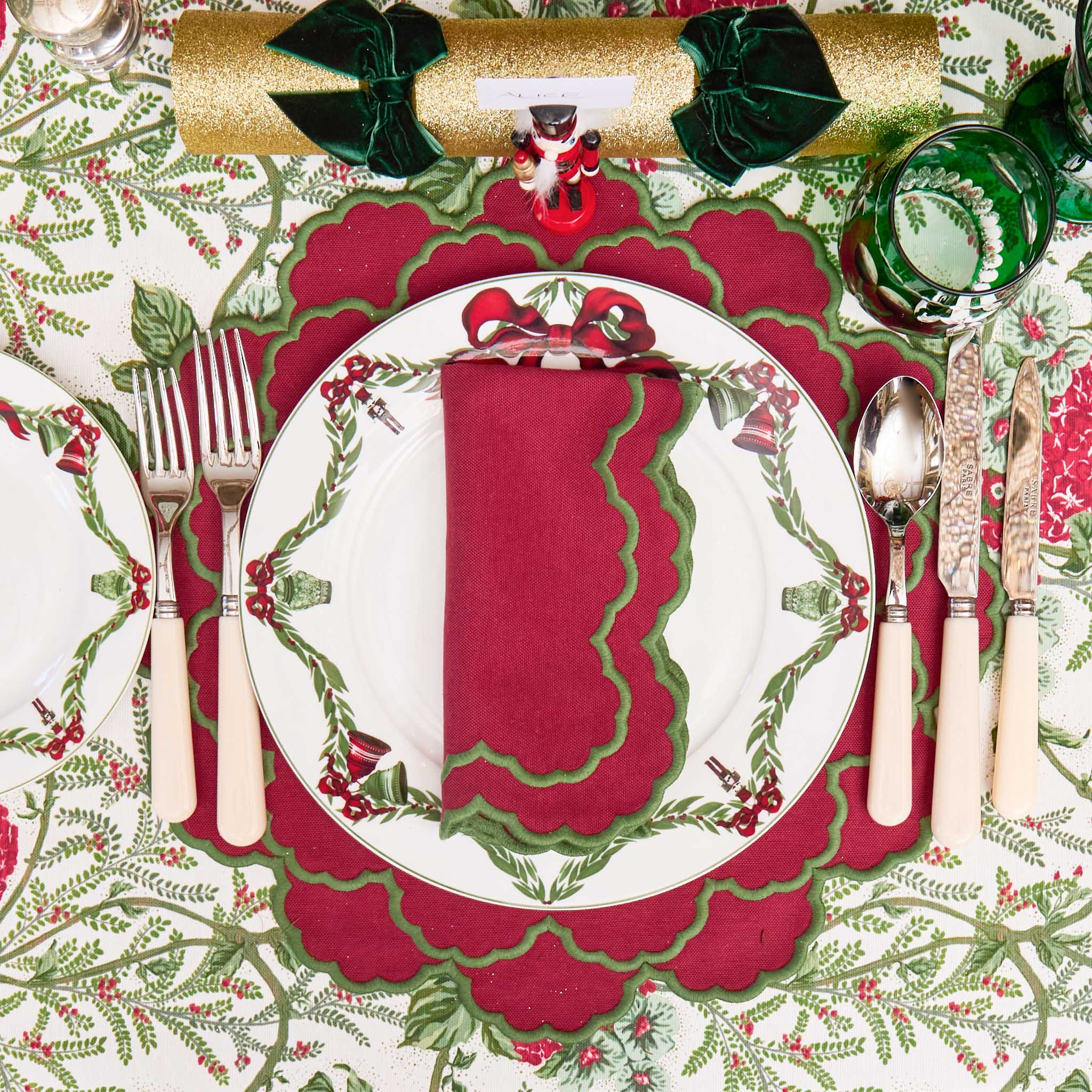Christmas-themed table setting with red and green decorations, including a plate, cutlery, and place mat.