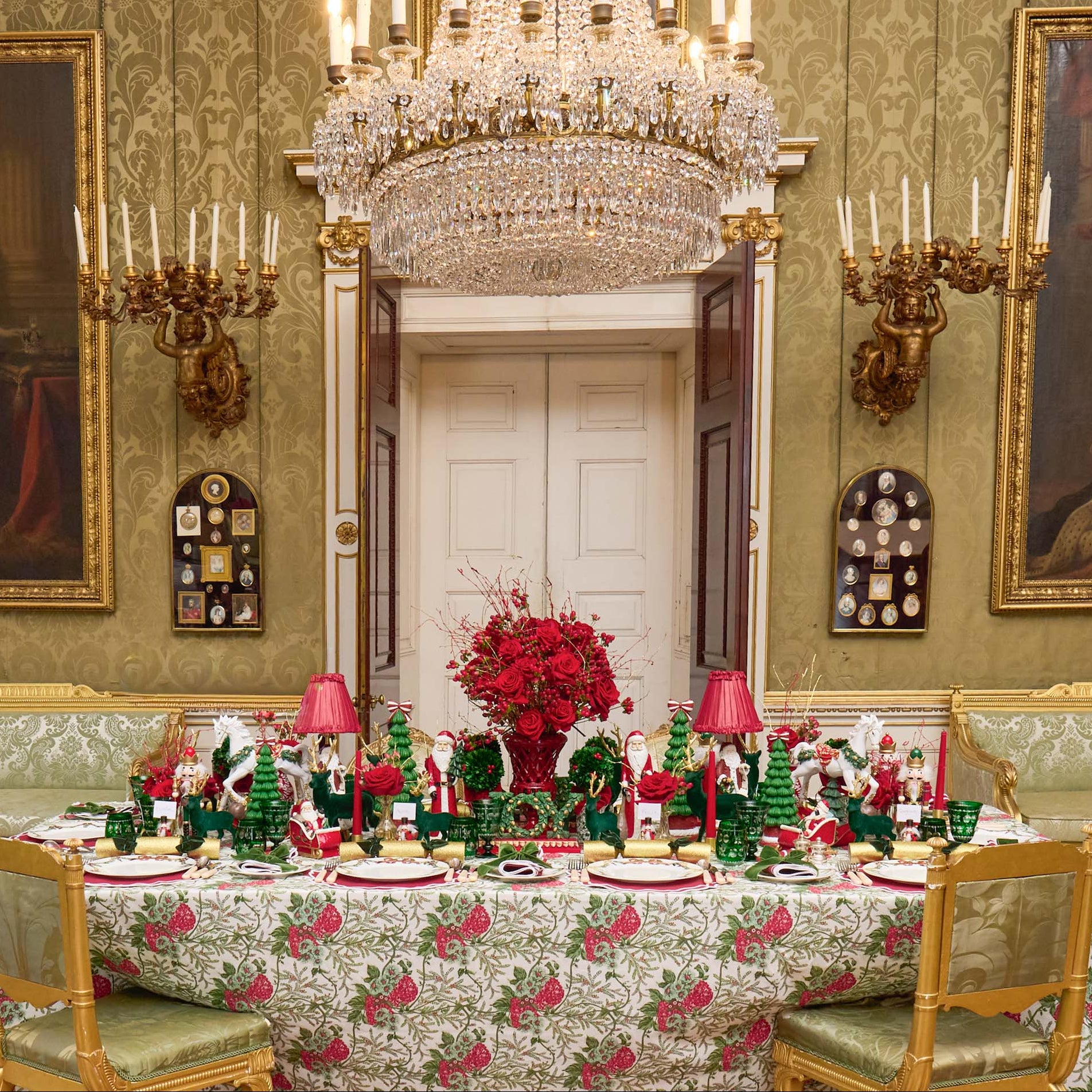 Decorative dining room with a table set for Christmas, featuring a large crystal chandelier and ornate wall decorations.