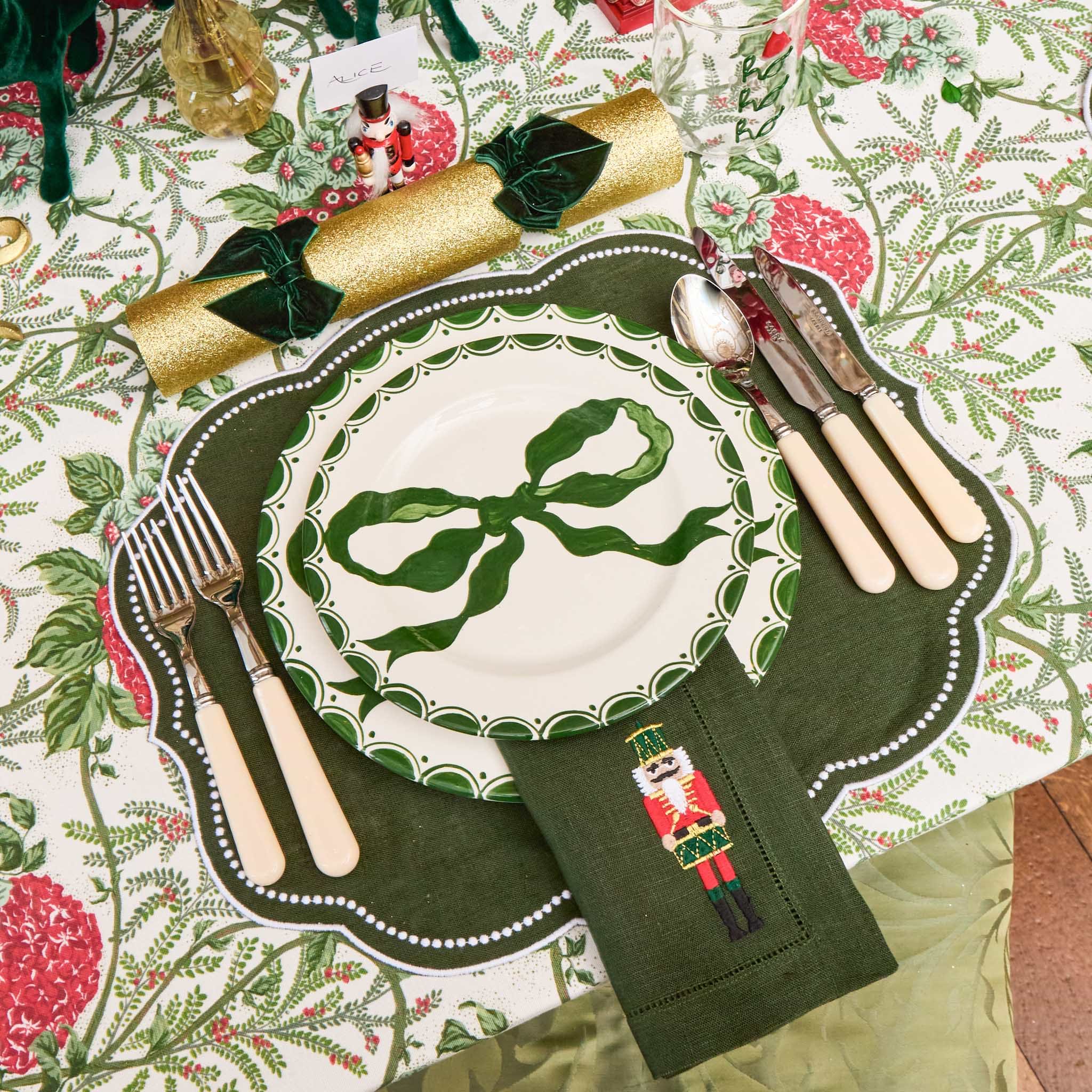 Christmas table setting with a plate, cutlery, and decorative napkin on a patterned tablecloth.