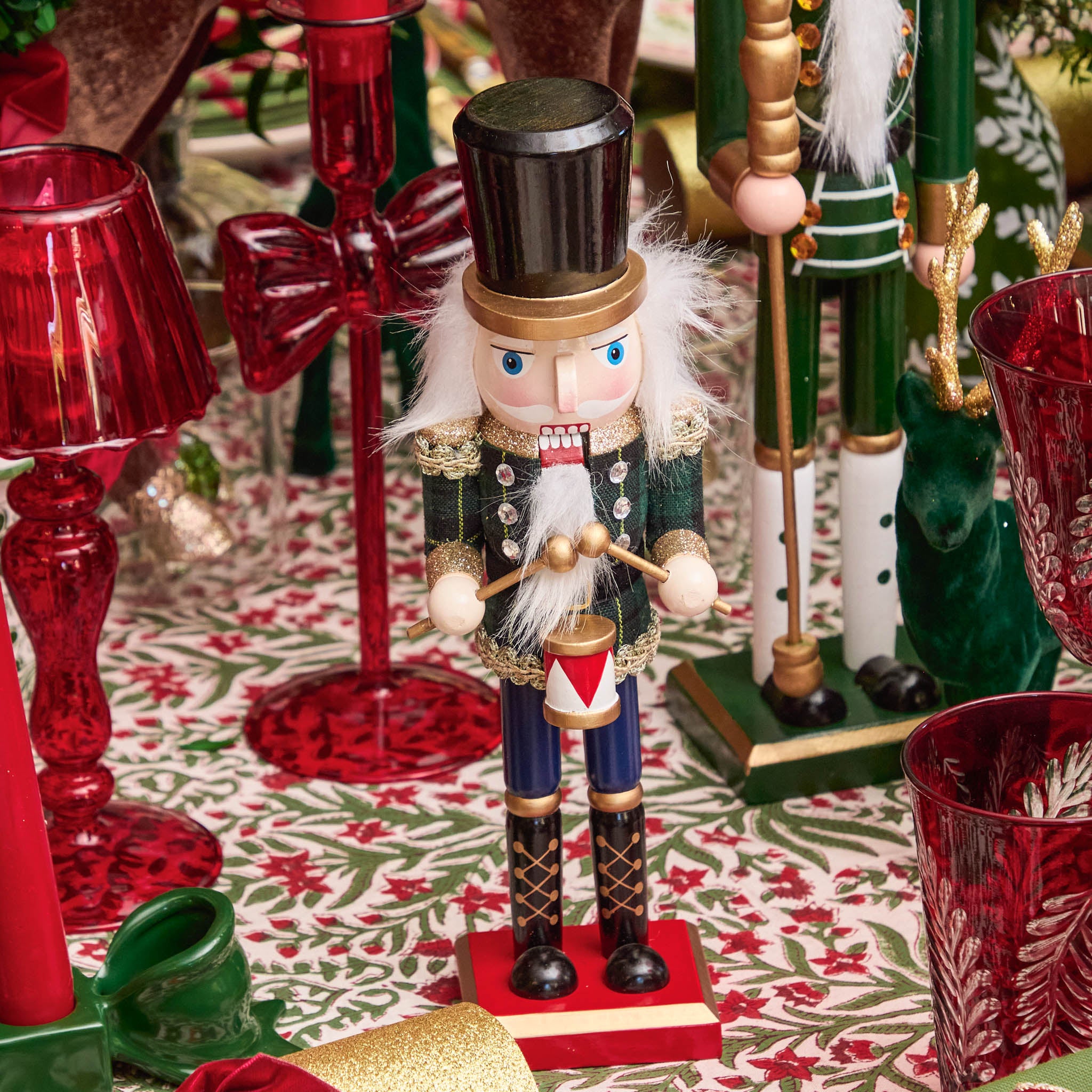Wooden nutcracker figure with red glass candle holders and a patterned tablecloth.