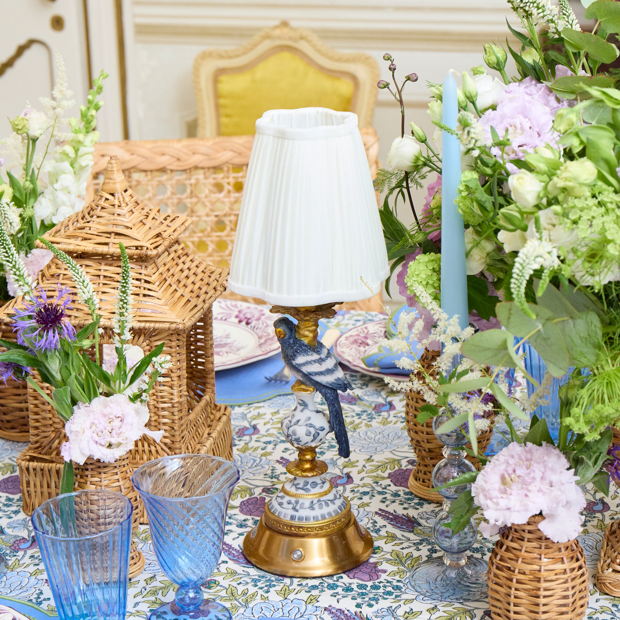 Decorative table setting with flowers, candles, and a lamp in a room with gold accents.