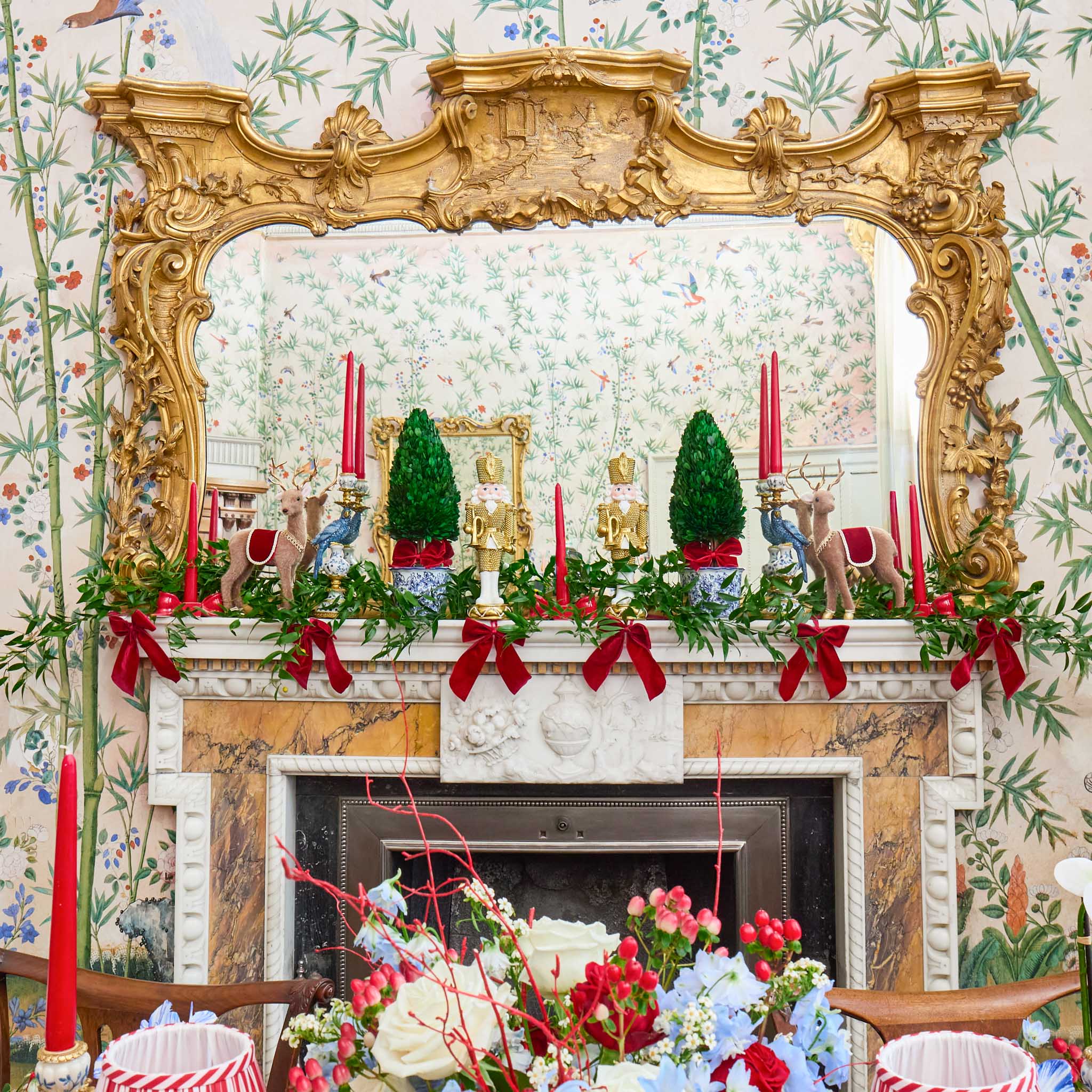 Decorative Christmas mantel with gold frame, candles, and greenery against floral wallpaper.