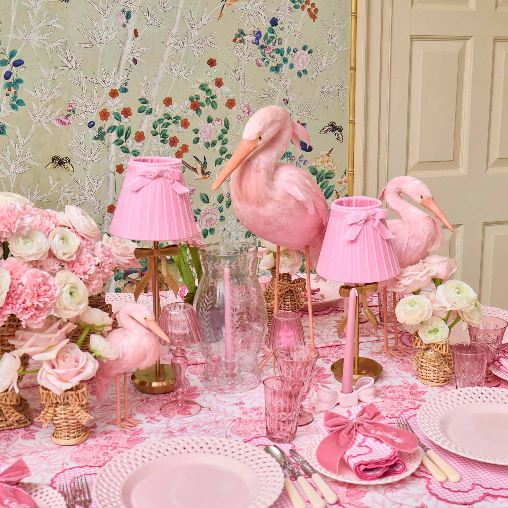 Pink flamingo decorations on a table with floral arrangements and pink tableware.