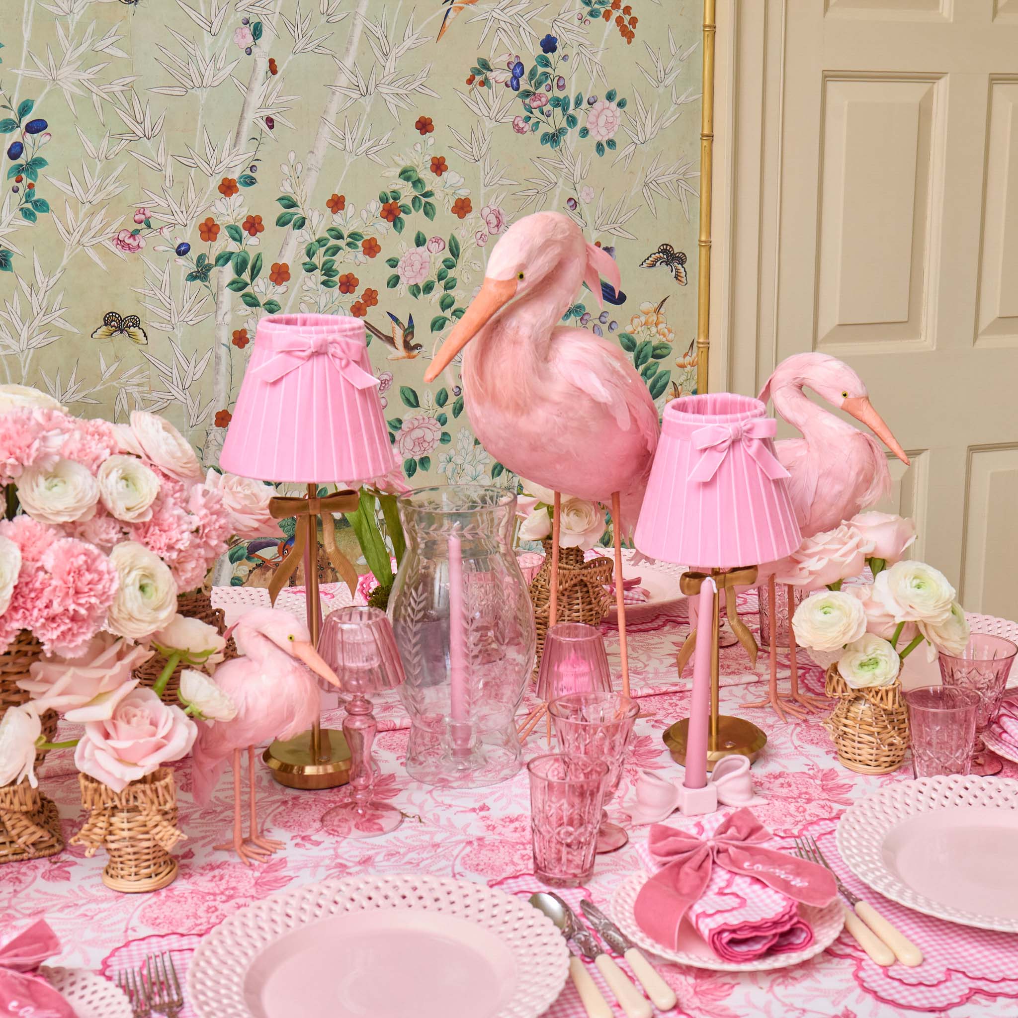 Pink flamingo decorations on a table with floral arrangements and pink tableware.
