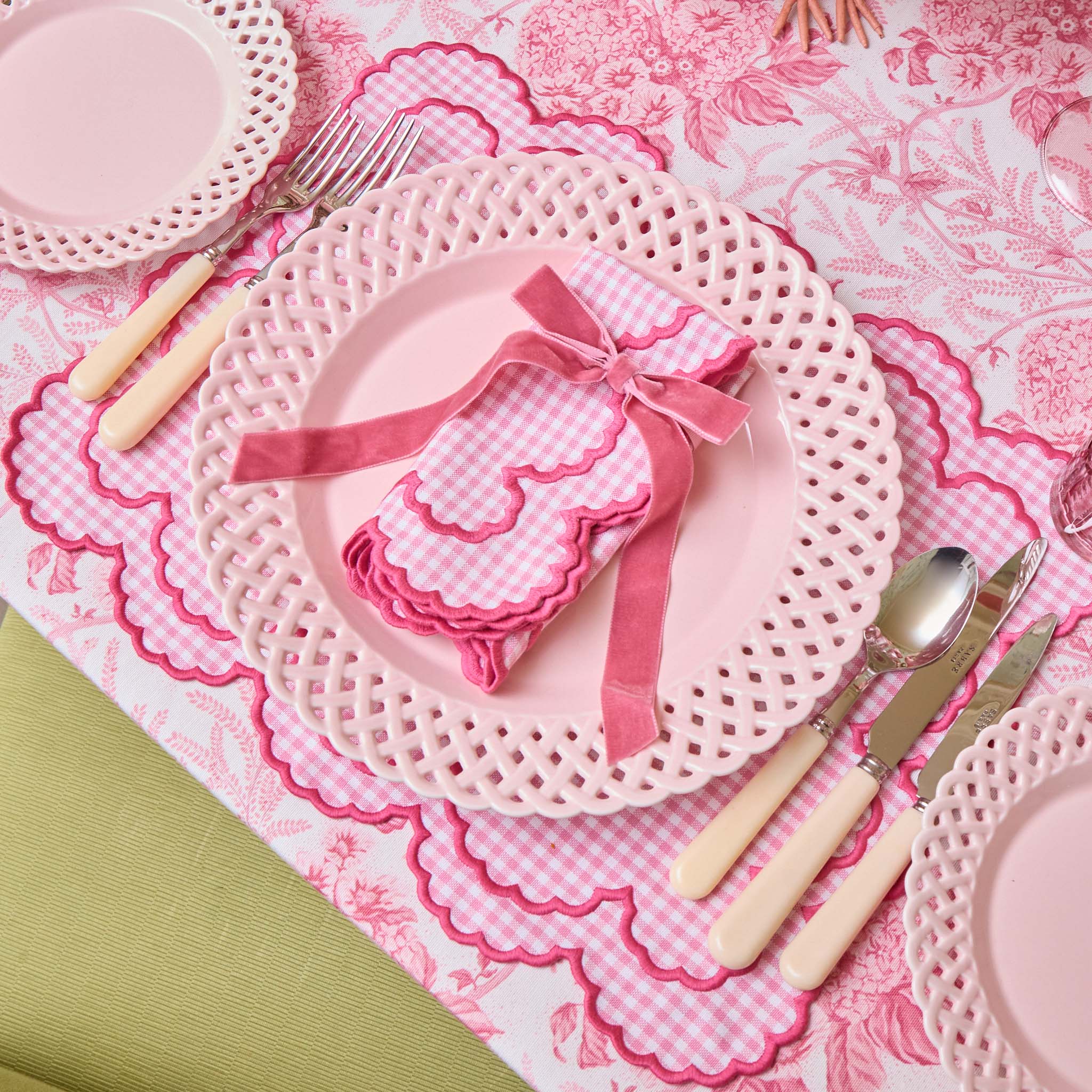 Pink table setting with plates, cutlery, and a decorative napkin on a matching pink tablecloth.