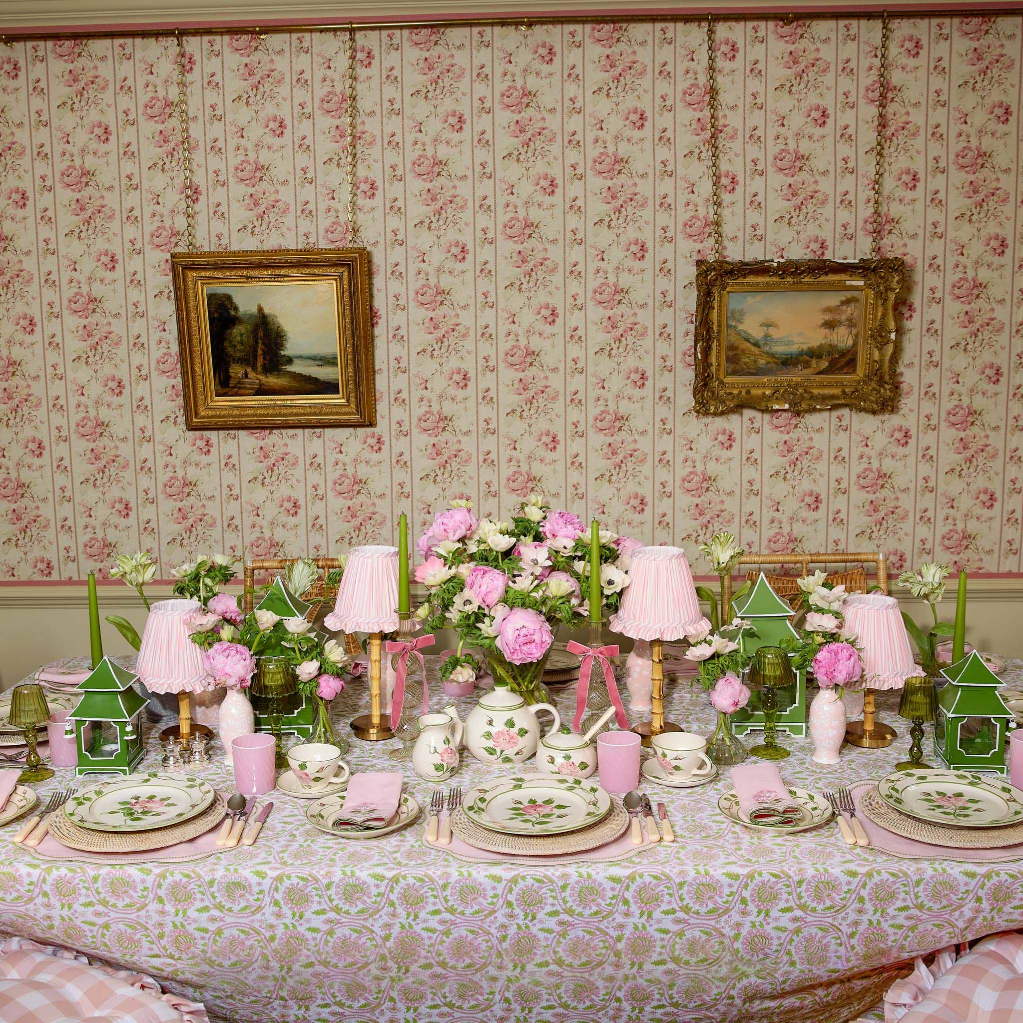 Decorative table setting with floral arrangements and tableware against a floral wallpapered wall.