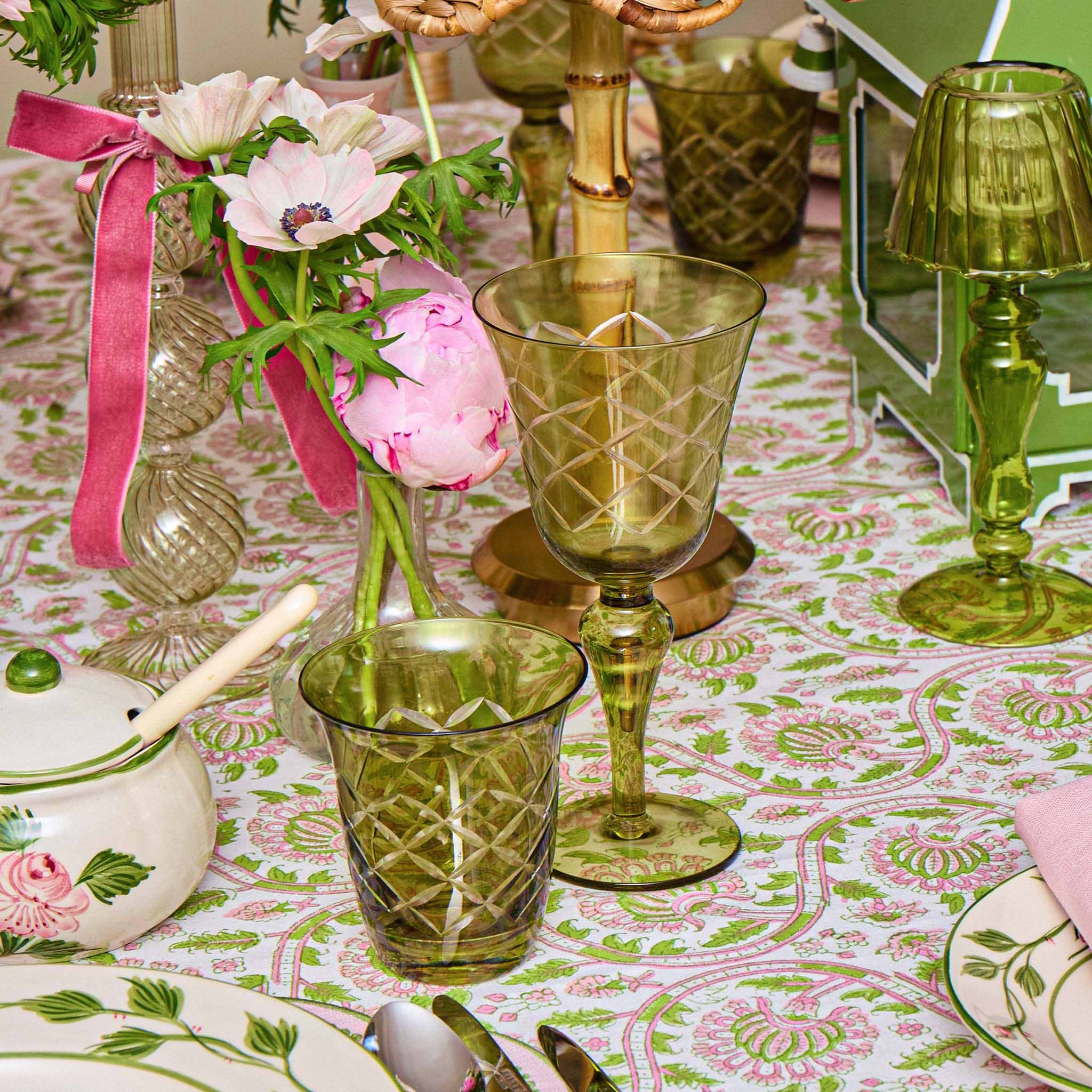 Decorative table setting with green glassware, pink flowers, and a patterned tablecloth.