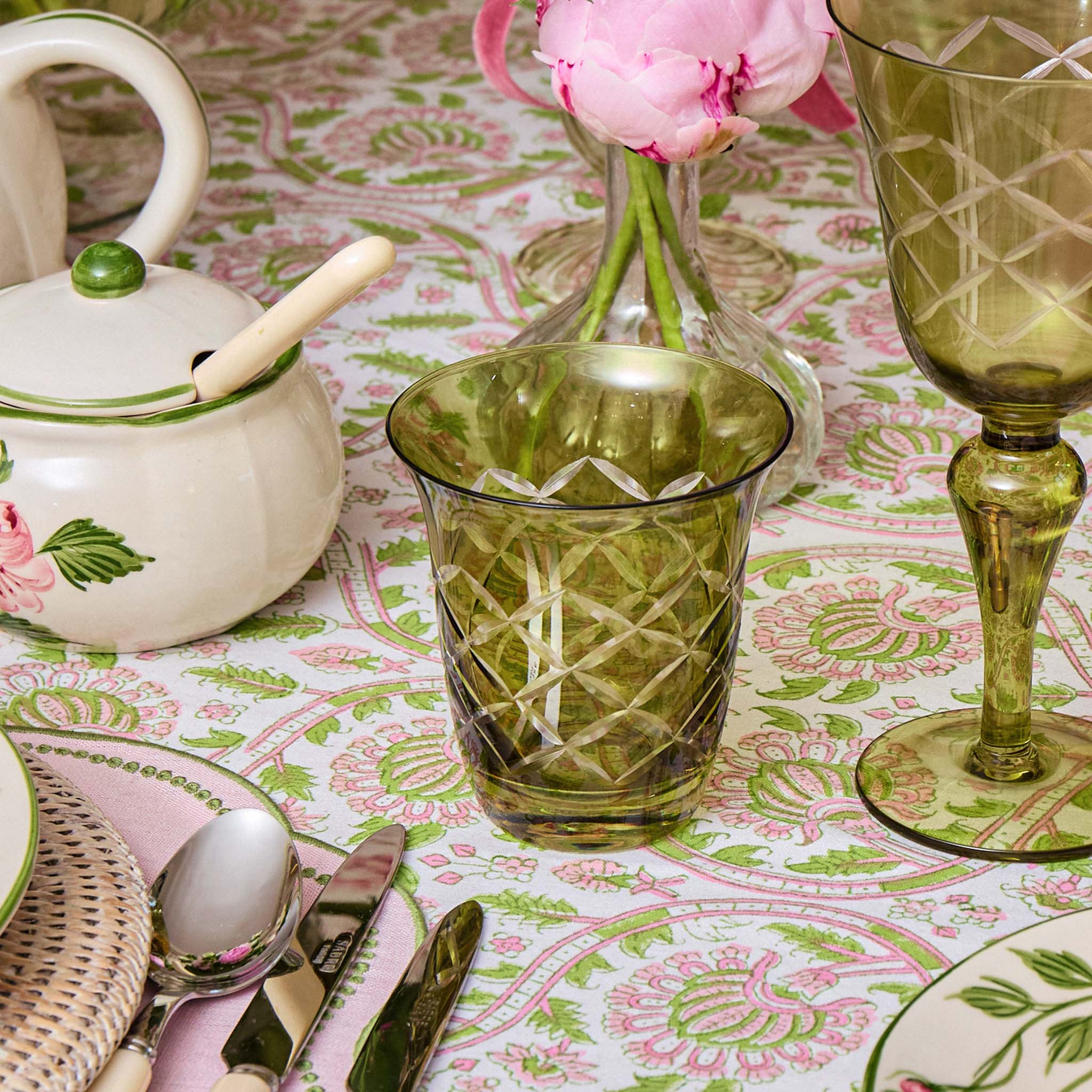 Table setting with green glassware, teapot, and floral tablecloth.