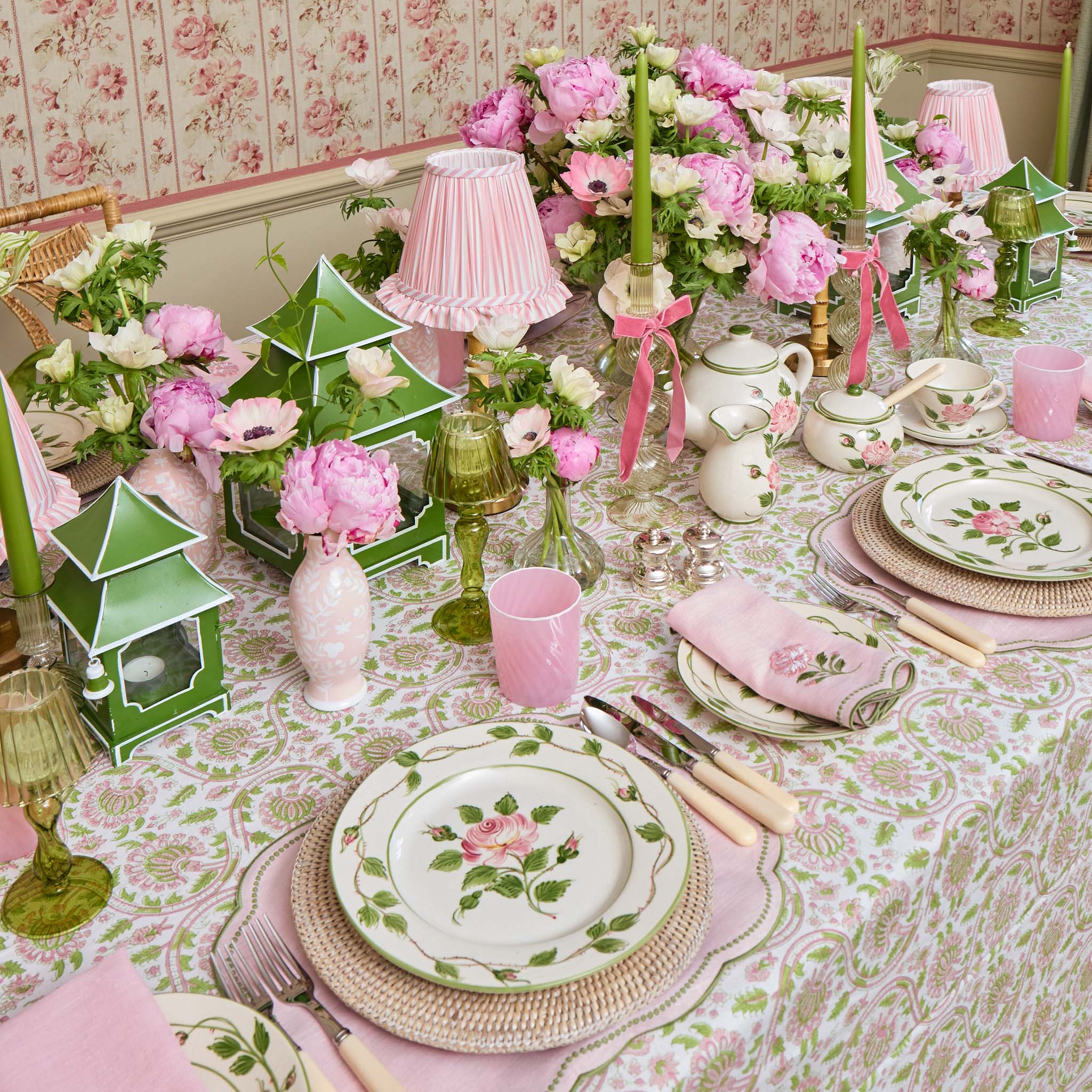 Decorative table setting with floral plates, pink cups, and green lanterns on a patterned tablecloth.