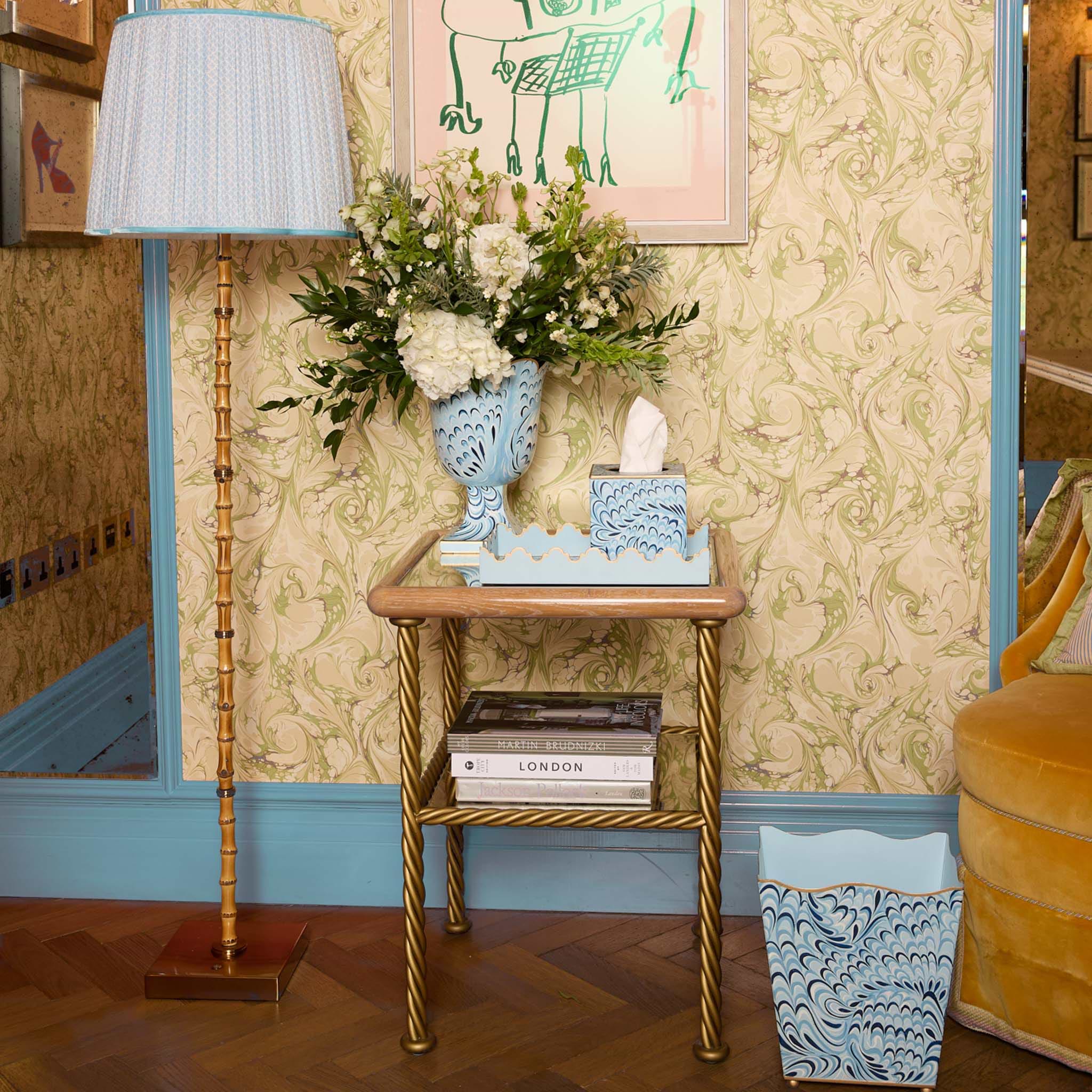 Decorative side table with floral arrangement, books, and decorative vases against a patterned wall.