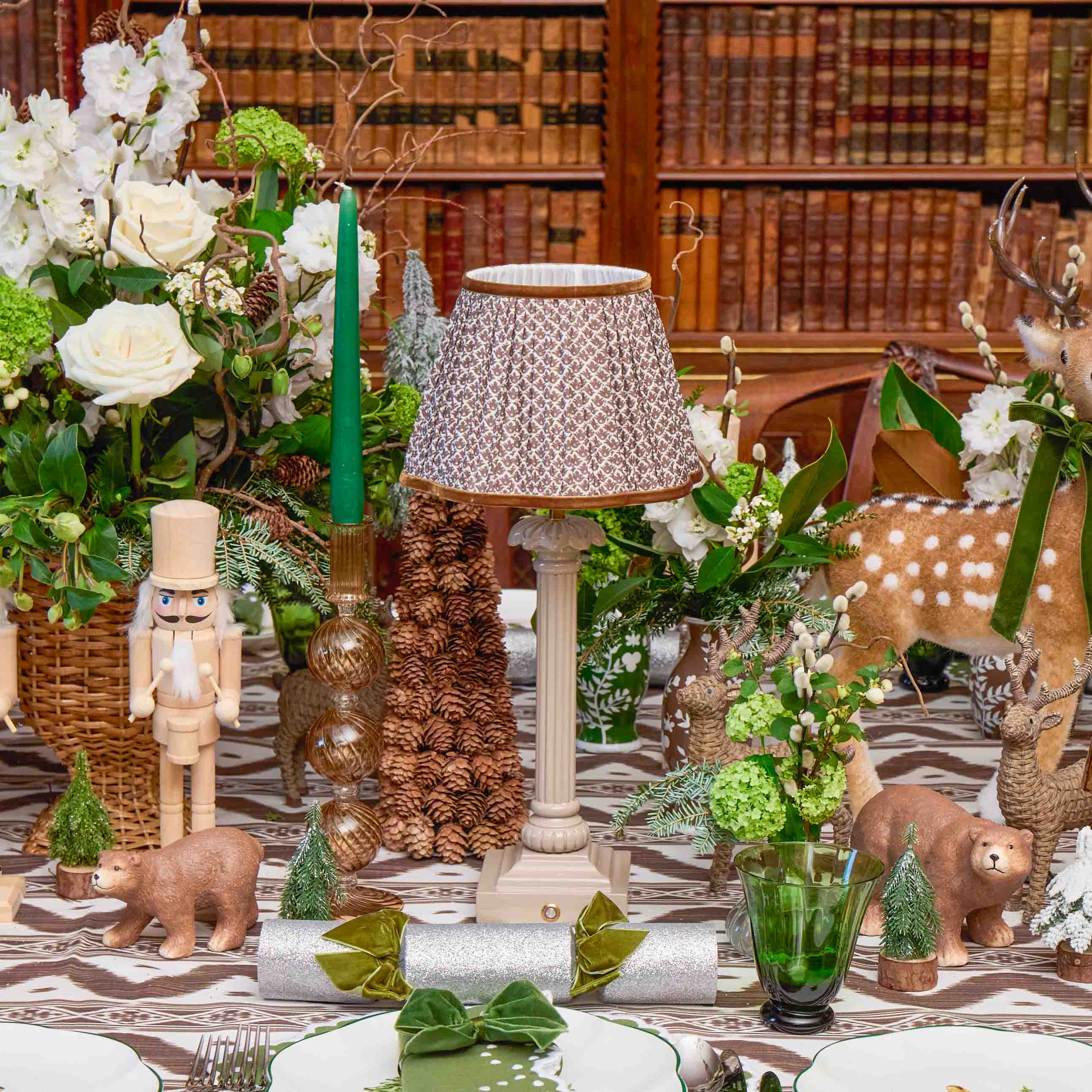 Decorative table setting with flowers, candles, and small figurines in a room with bookshelves.