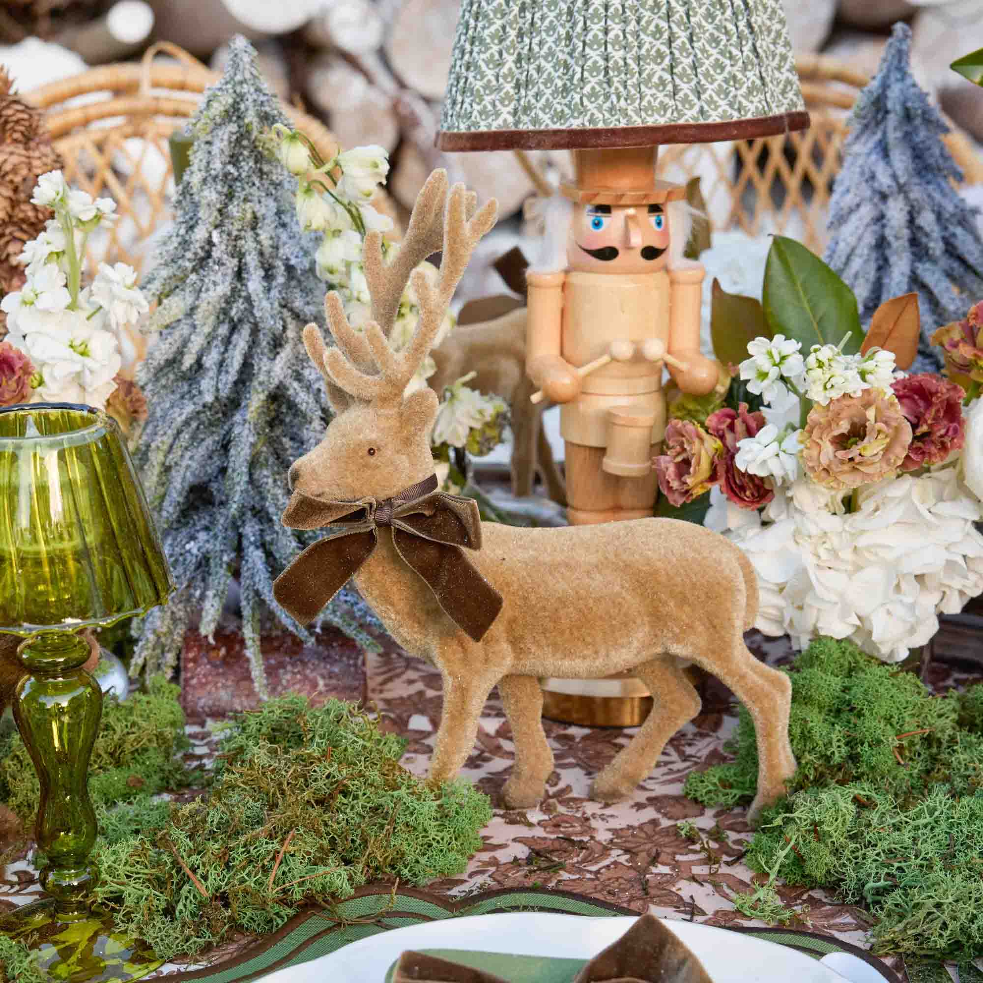 Decorative table setting with a deer figurine, nutcracker, and floral arrangement.