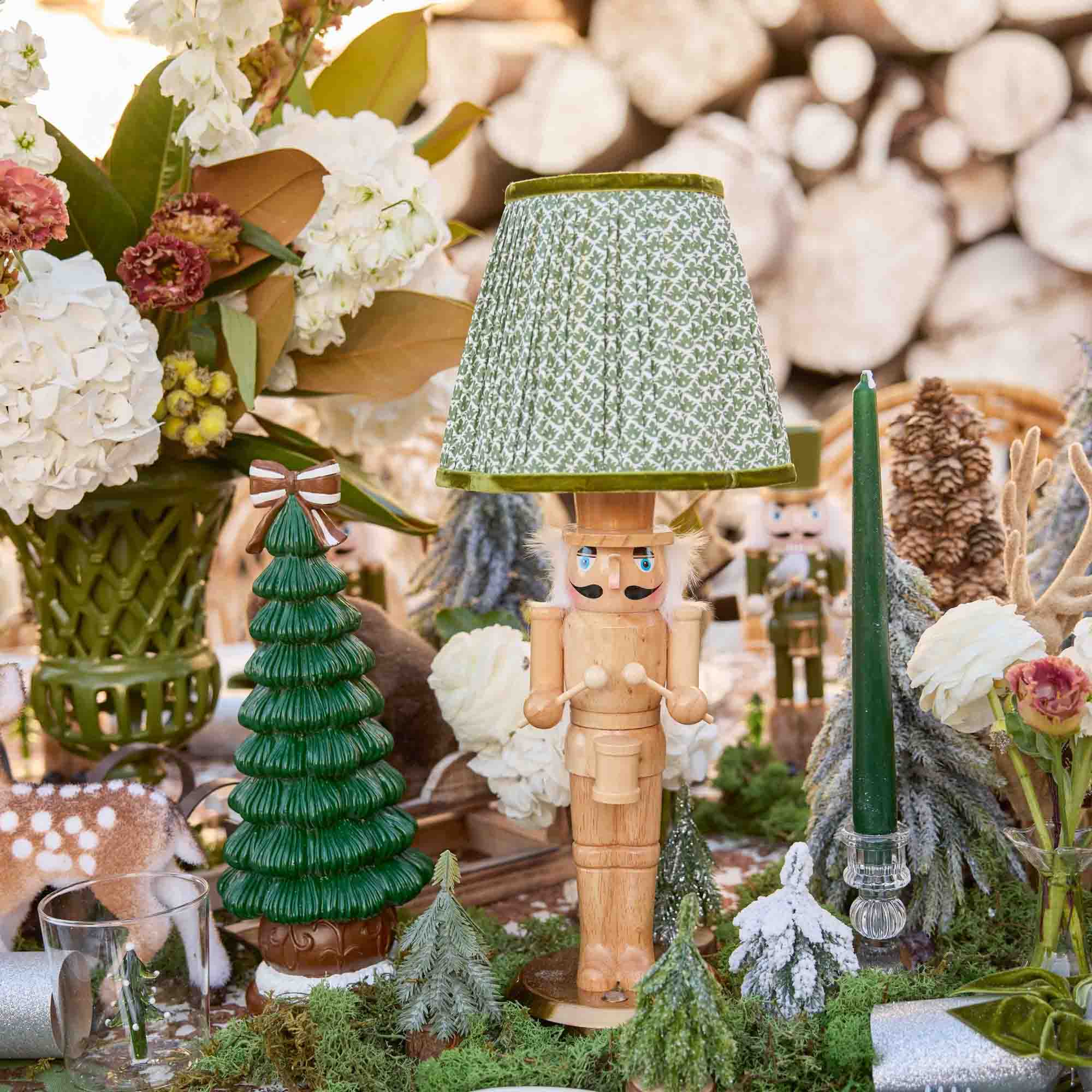 Decorative table setting with a nutcracker, Christmas trees, and flowers against a stone wall.