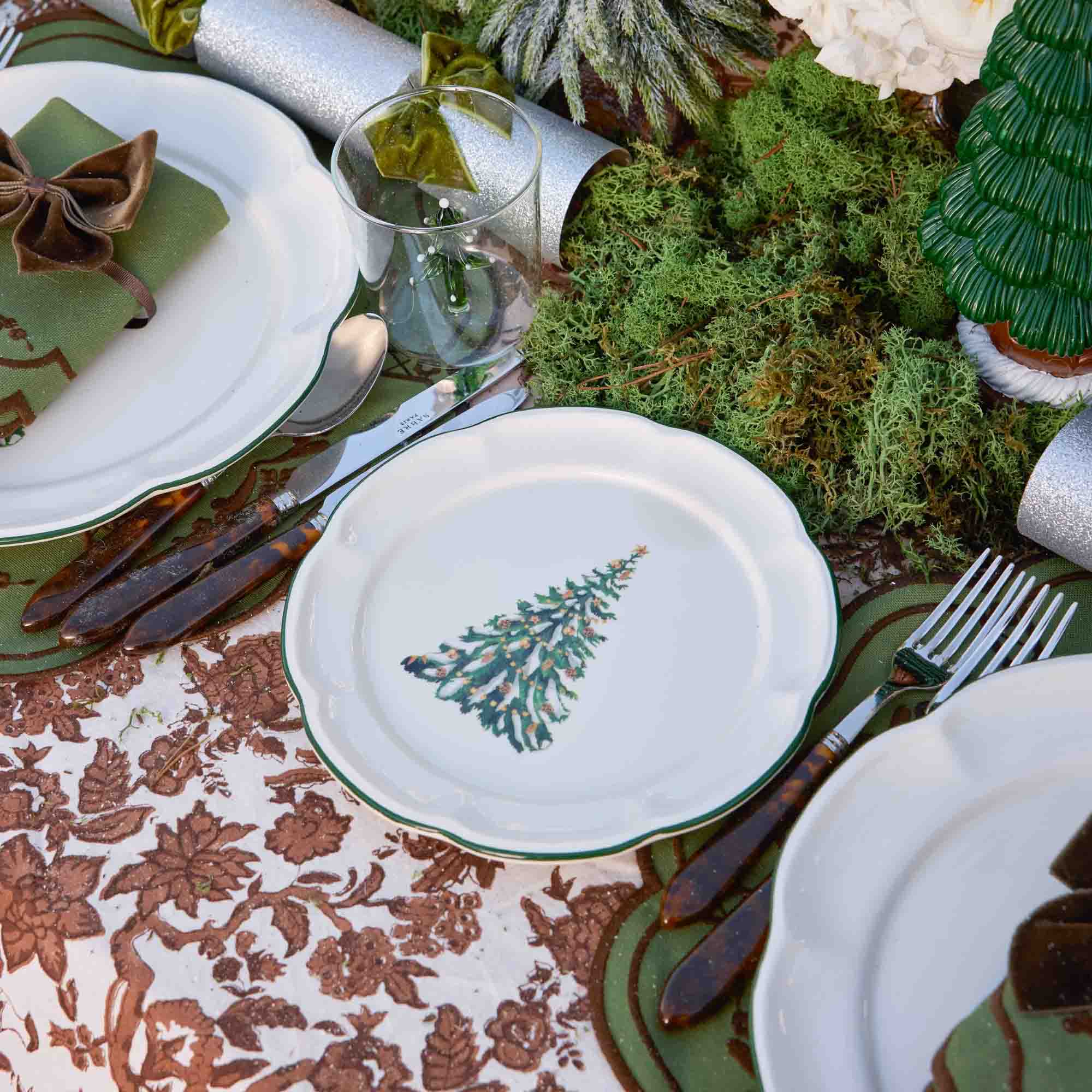 Christmas-themed table setting with decorative plates, silverware, and a floral tablecloth.