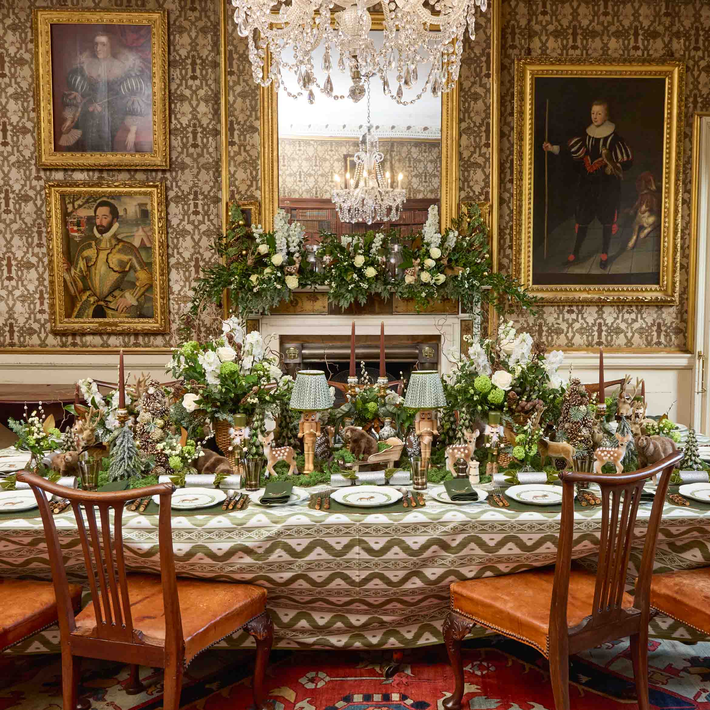 Decorative dining table set with floral arrangements in an ornate room with portraits and a chandelier.