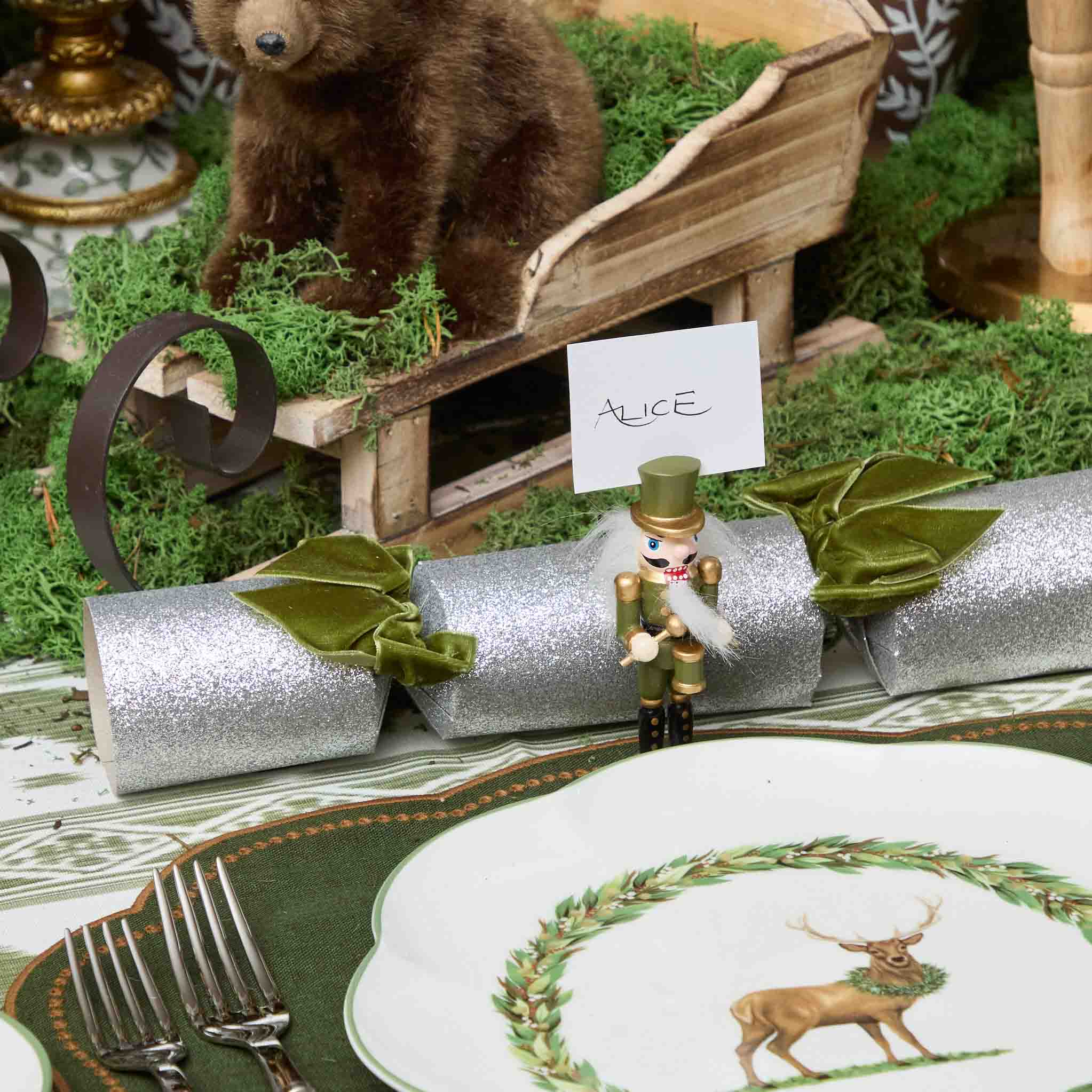 Decorative table setting with a bear figurine, nutcracker, and Christmas cracker on a green and gold tablecloth.