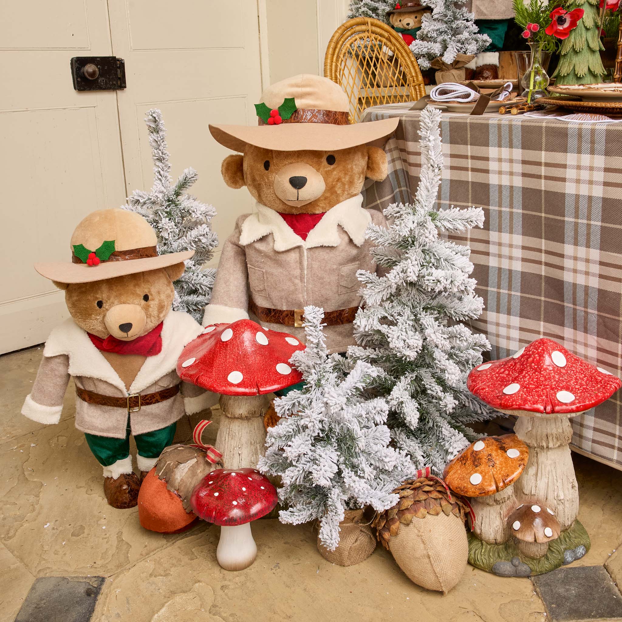 Two teddy bears in festive attire with decorative mushrooms and trees on a checkered tablecloth.