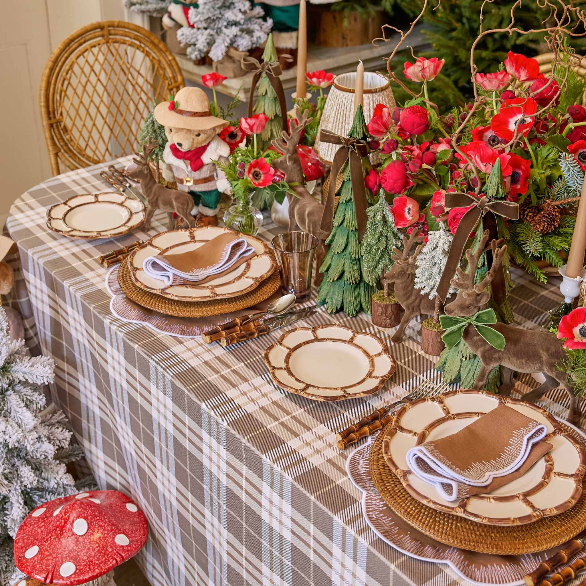 Decorative table setting with plaid tablecloth, wooden plates, and festive decorations including a bear figurine and red flowers.