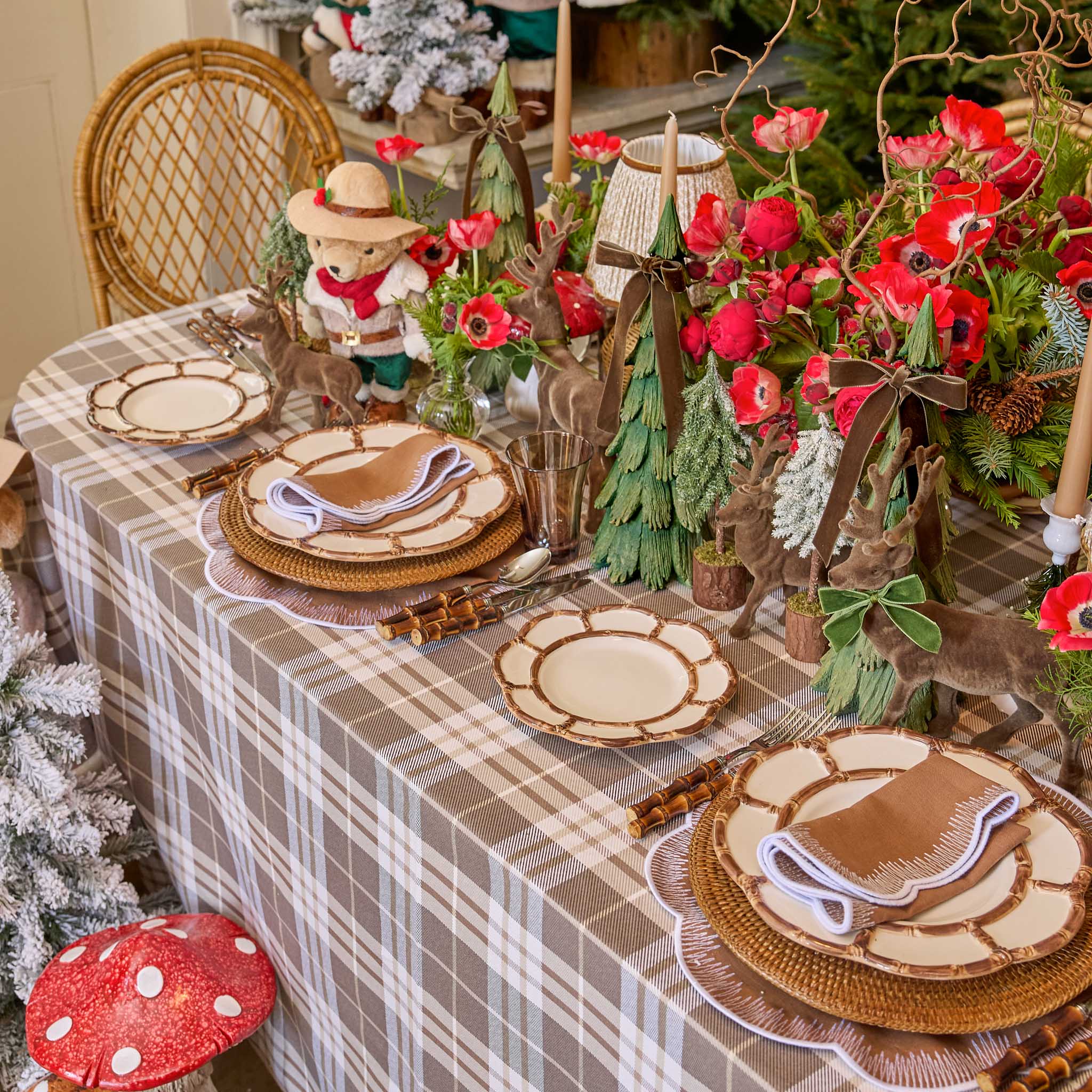 Decorative table setting with plaid tablecloth, wooden plates, and festive decorations including a bear figurine and red flowers.