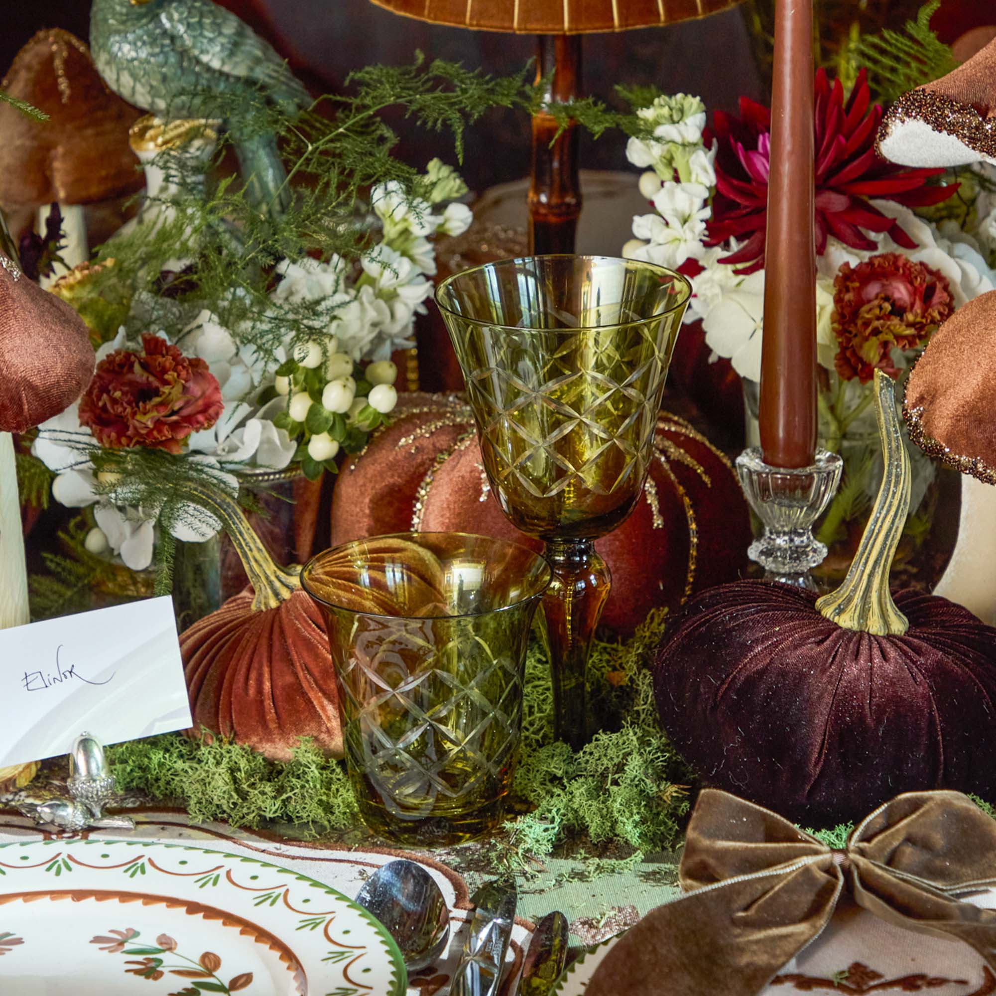 Decorative table setting with pumpkins, glasses, and flowers on a tablecloth.