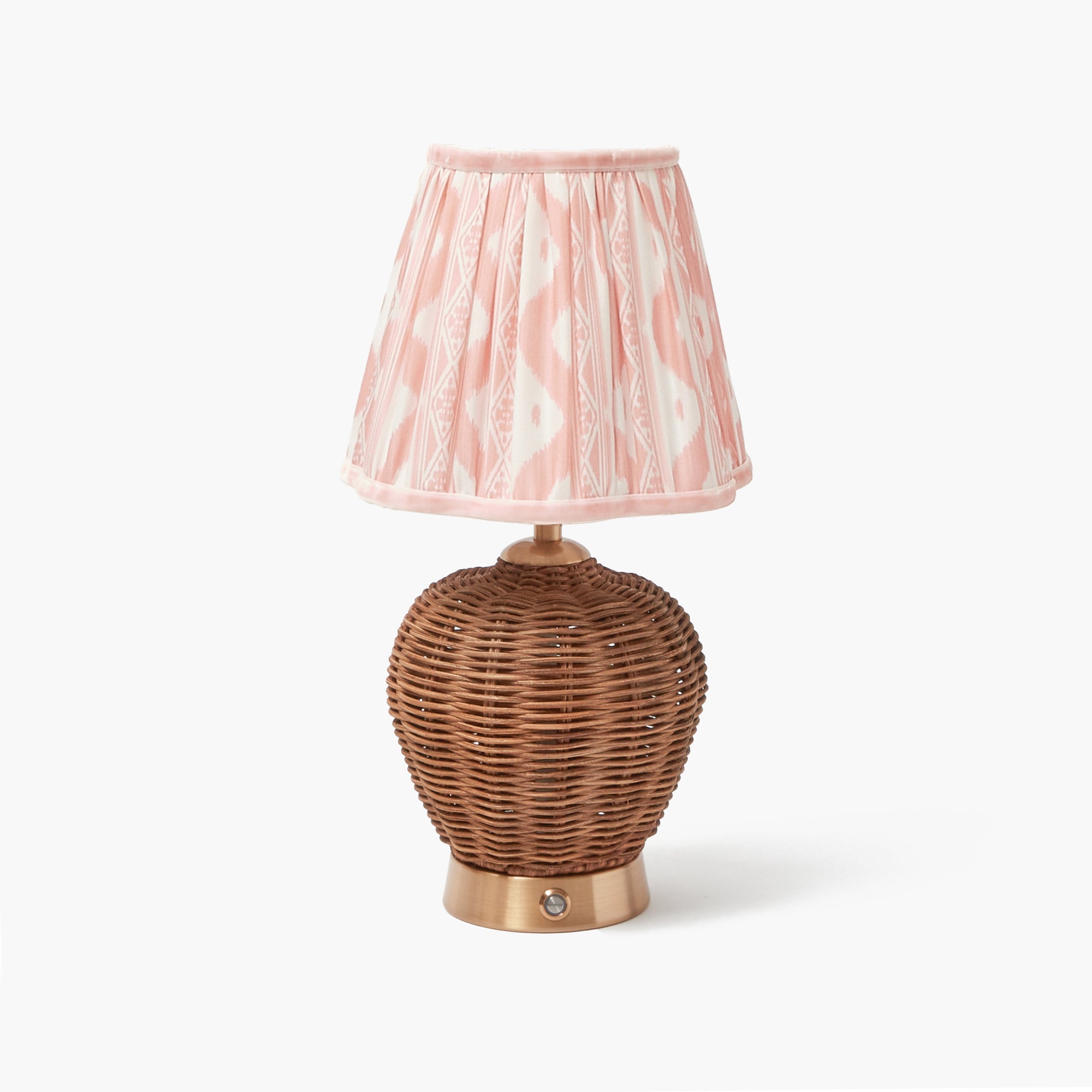 A brown rattan rechargeable lamp base with a pink ikat lampshade, standing on a gold platform.