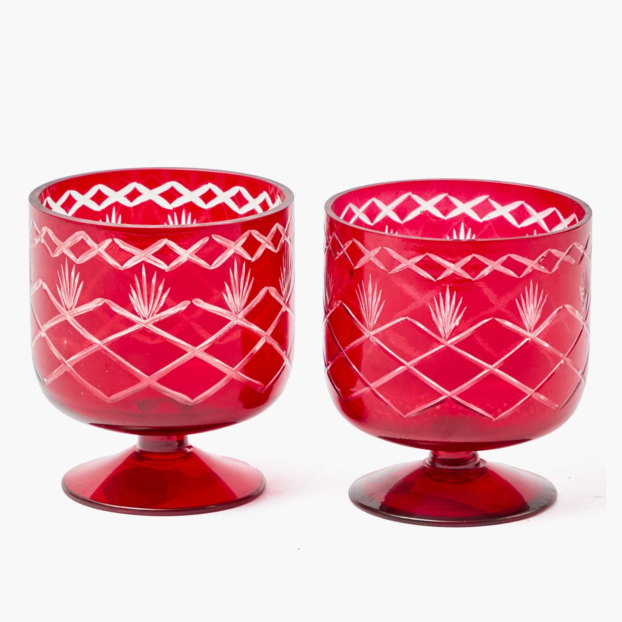 Two red glass tumblers with white geometric patterns on a white background