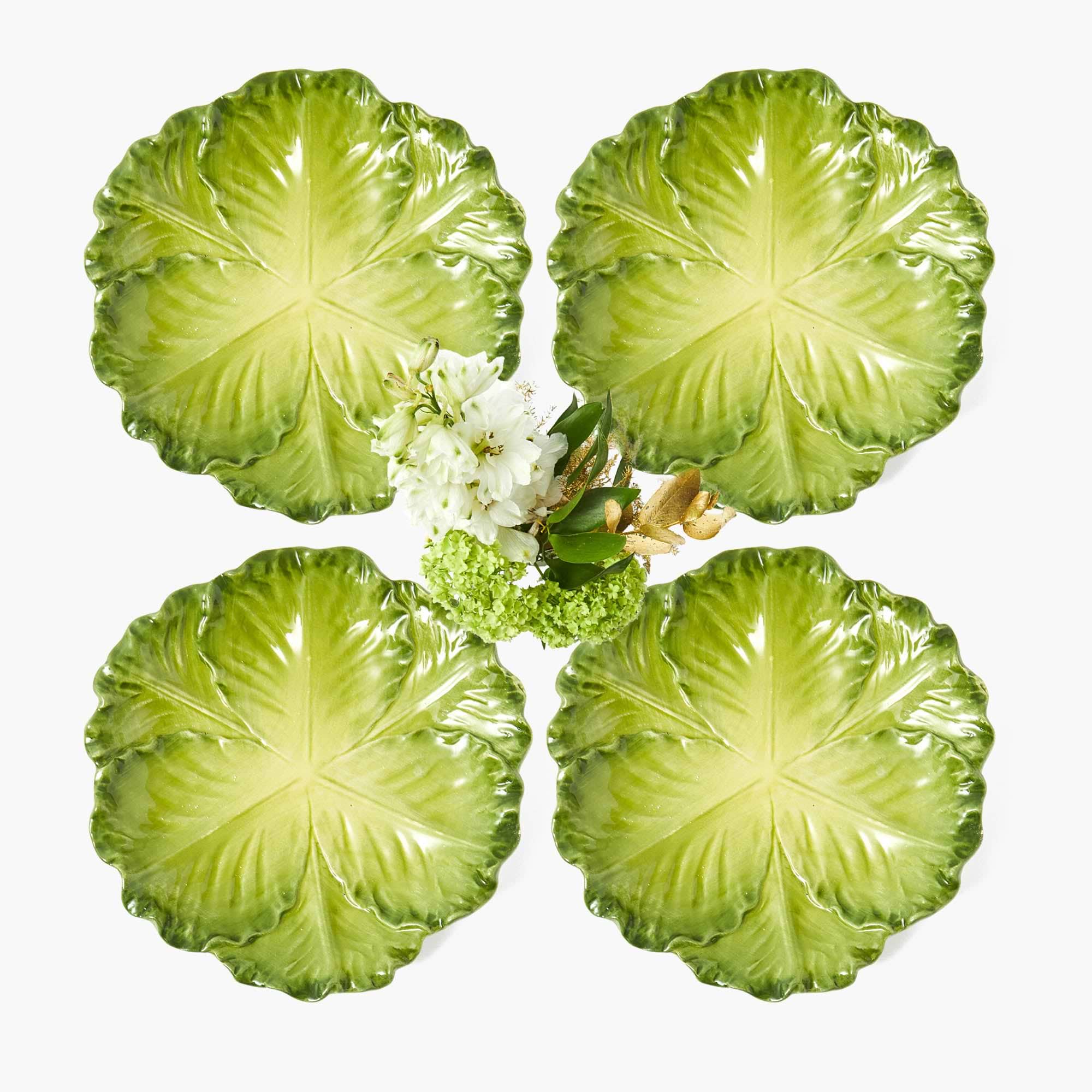 A set of four green cabbage-shaped ceramic plates with a hand-painted design, displayed with a floral centerpiece.
