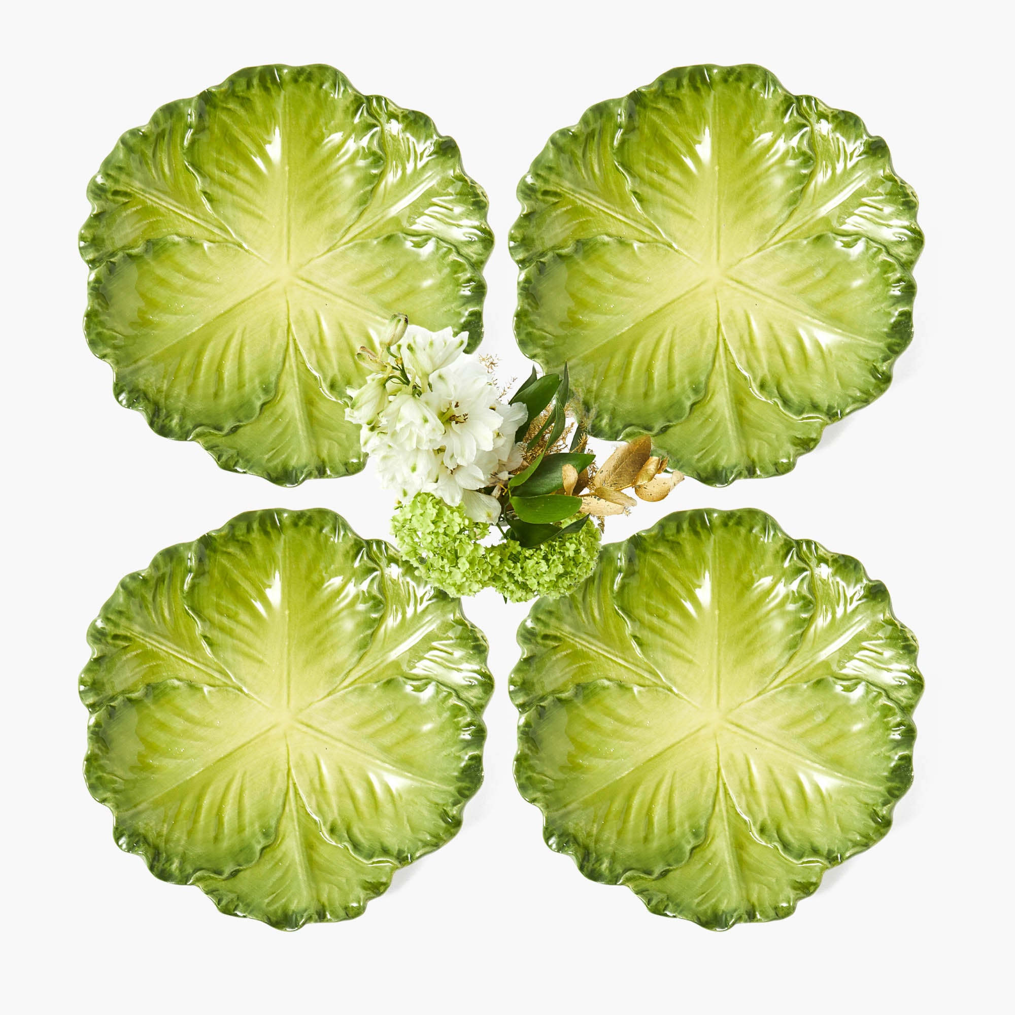 A set of four green cabbage-shaped ceramic plates with a hand-painted design, displayed with a floral centerpiece.