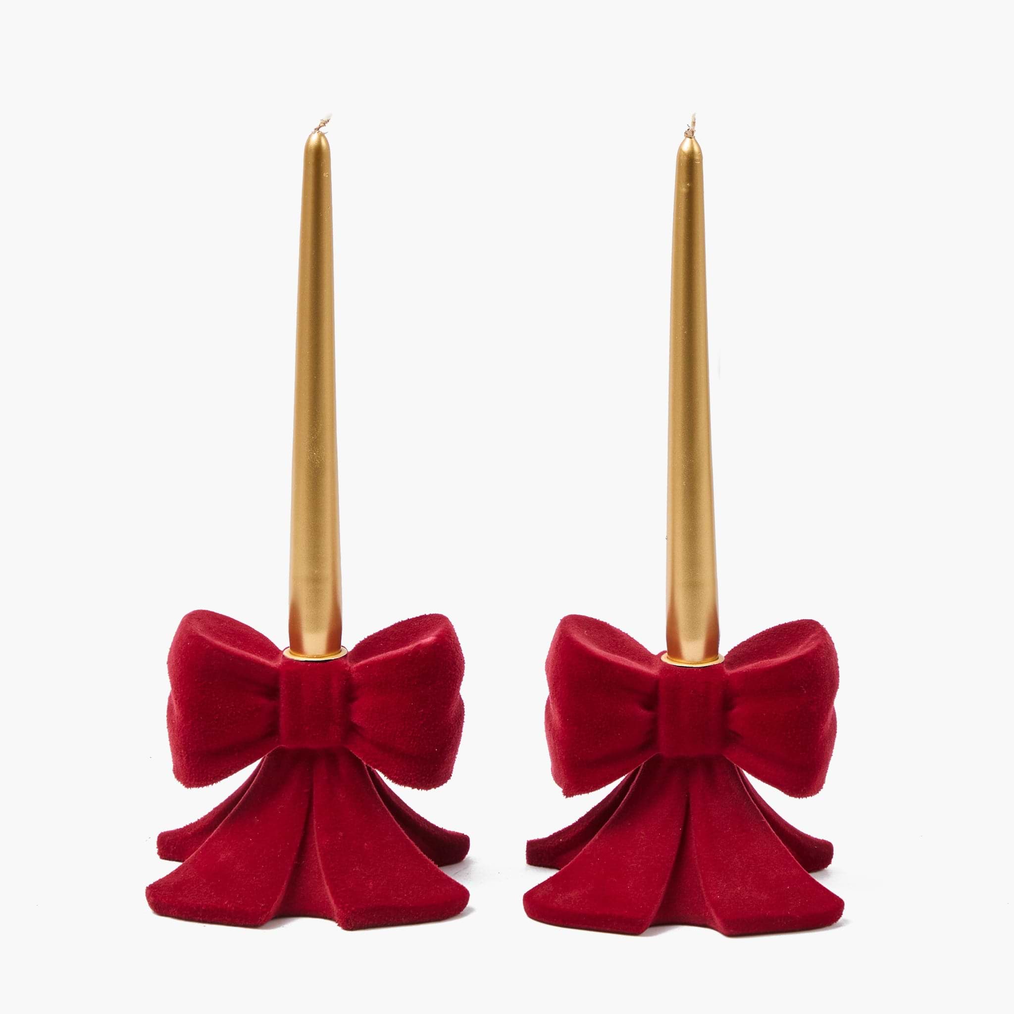 Two red velvet bow candle holders with gold candles on a white background