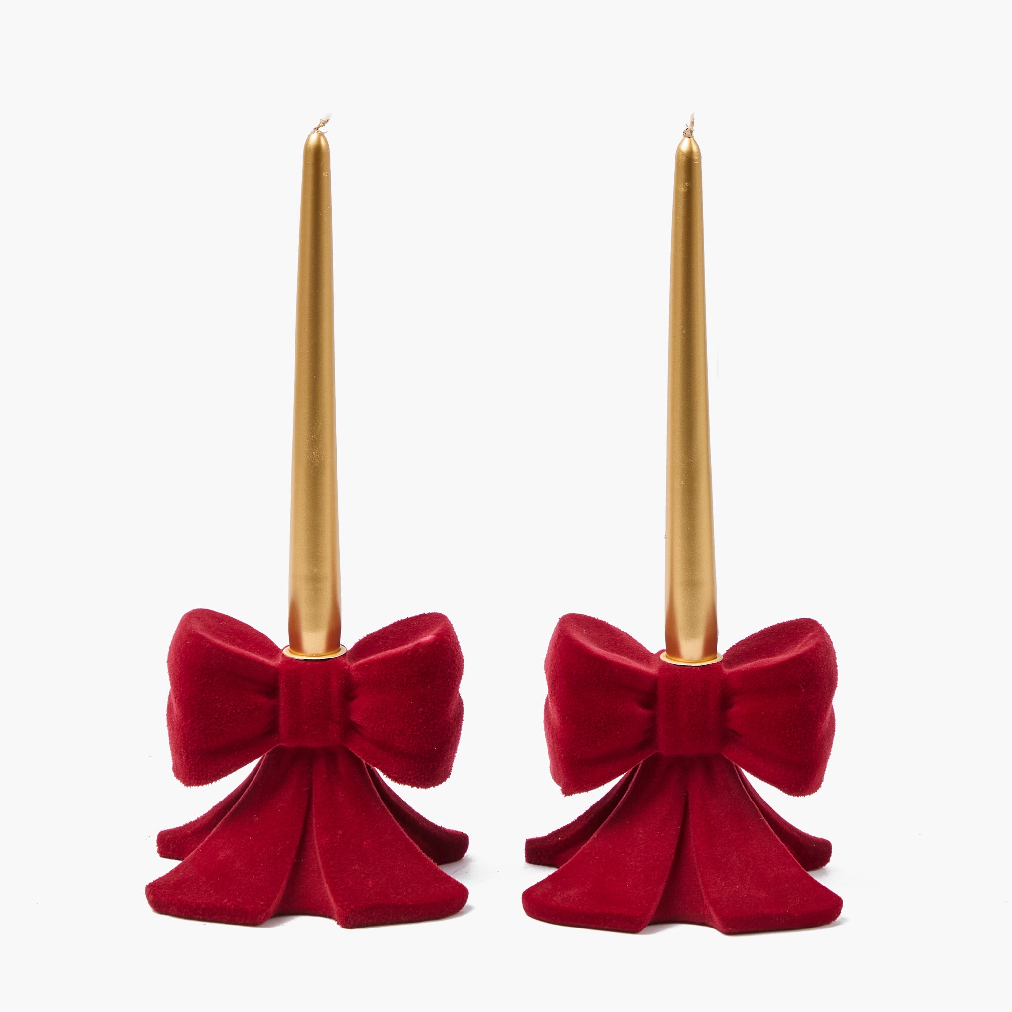 Two red velvet bow candle holders with gold candles on a white background