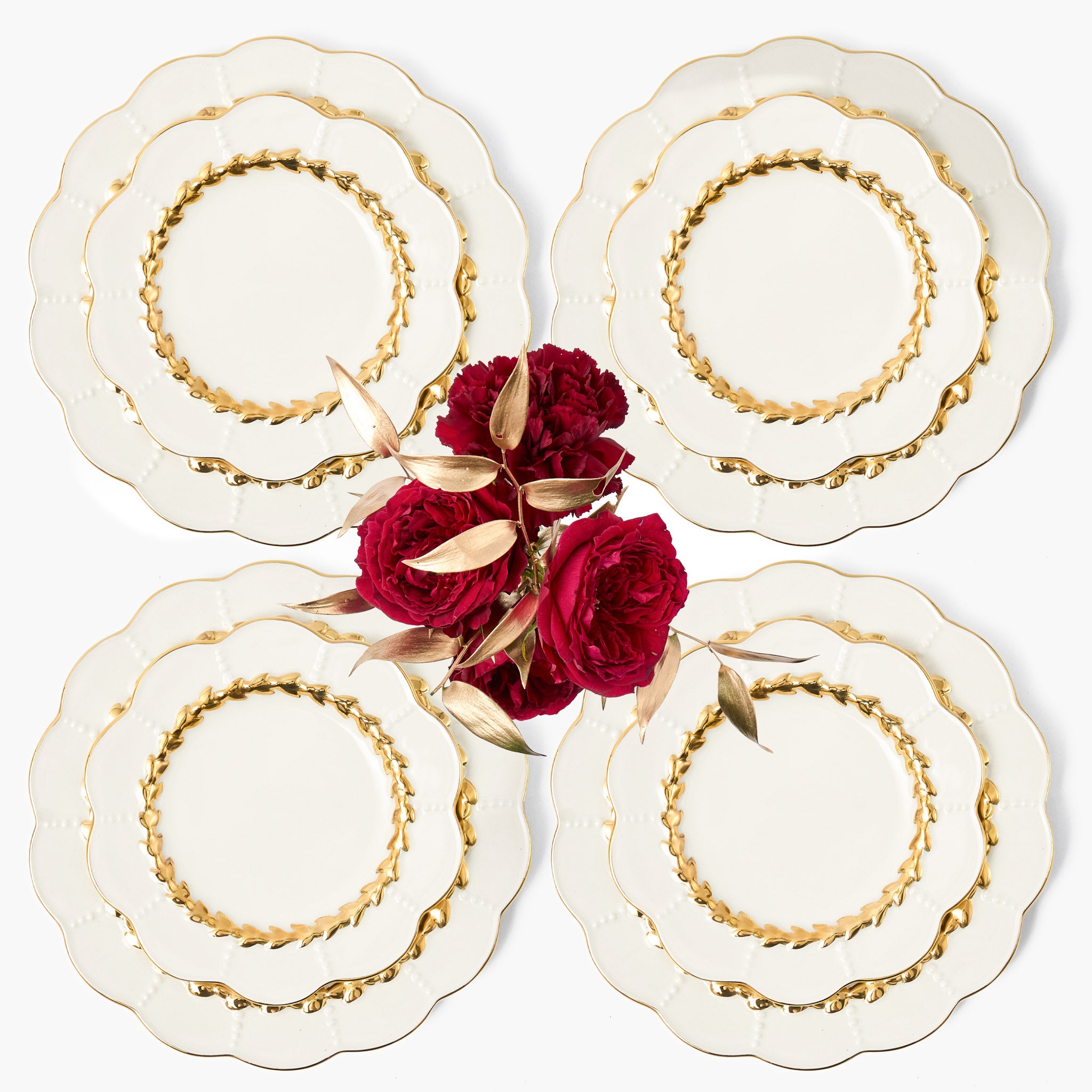 Set of four decorative plates with gold rims and red flowers in the center on a white background