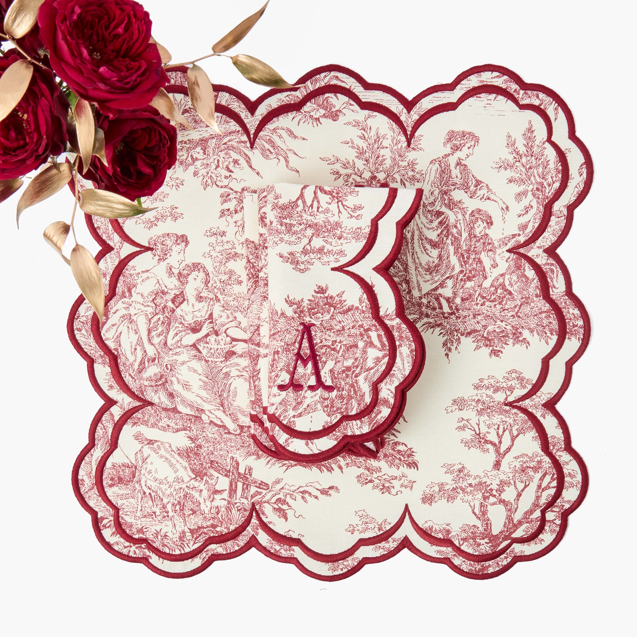 Decorative red and white doily with floral design and 'A' monogram, placed on a white surface with red roses.