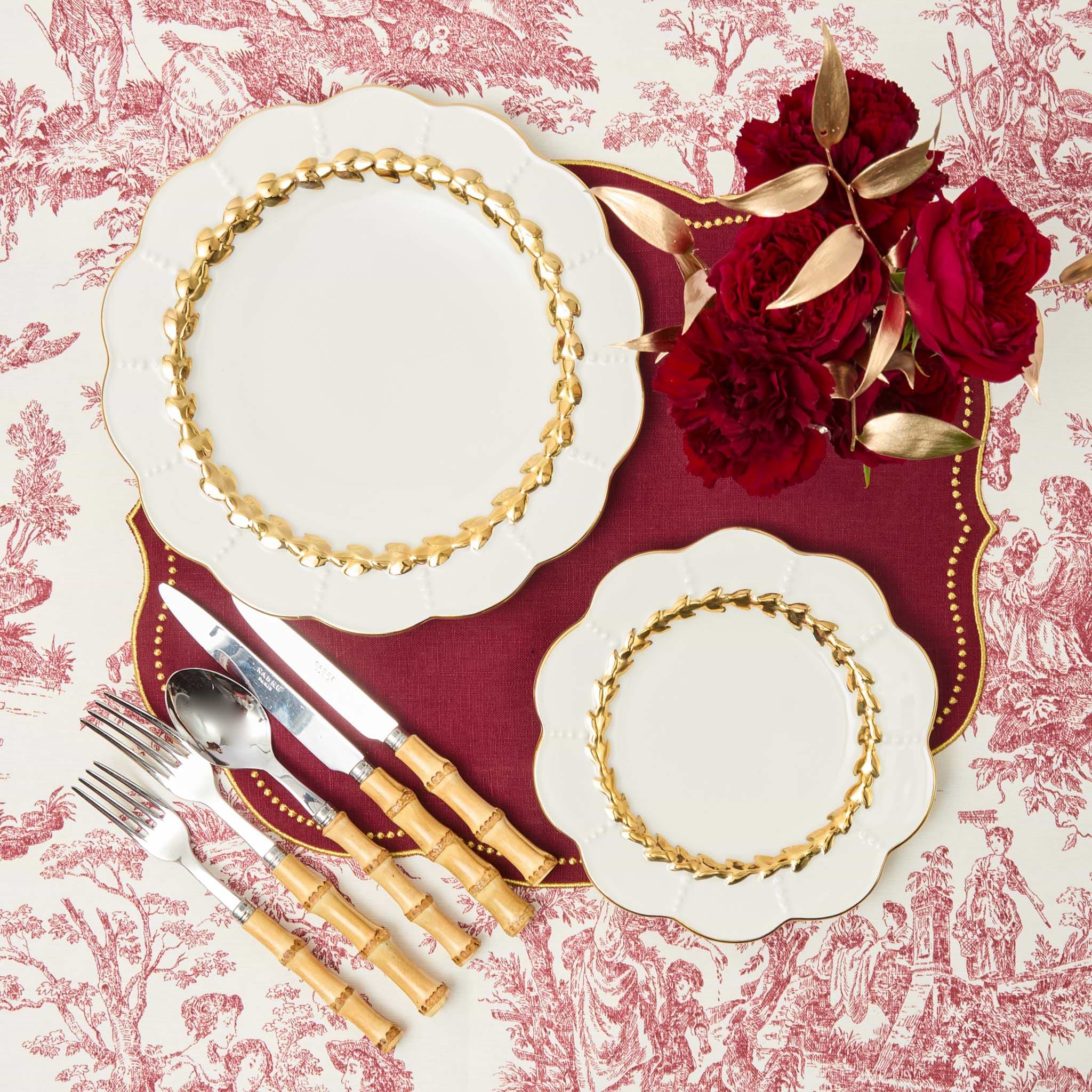 Decorative christmas table setting with gold-rimmed plates, red roses, and silverware on a patterned tablecloth.