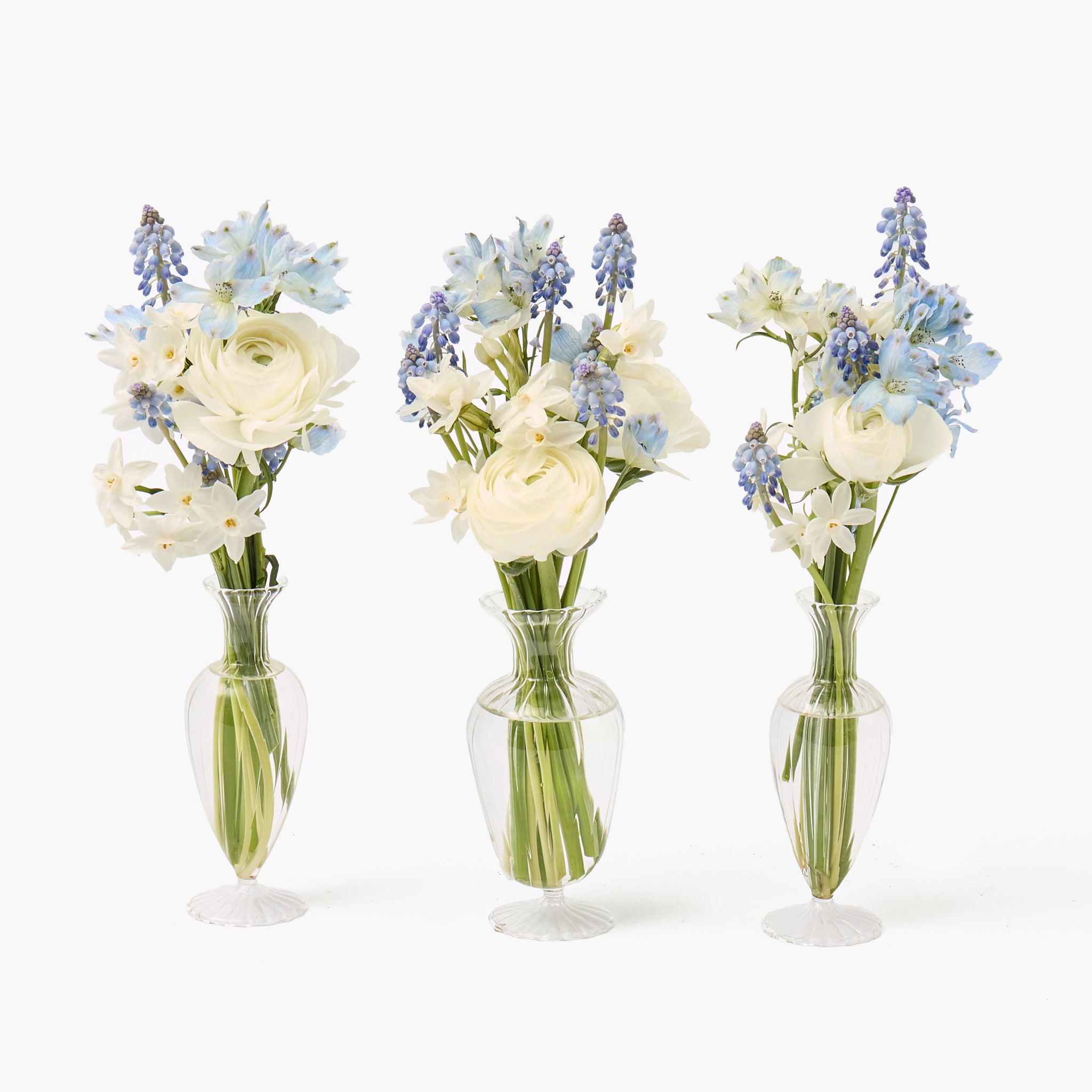 Three floral arrangements in clear vases on a white background