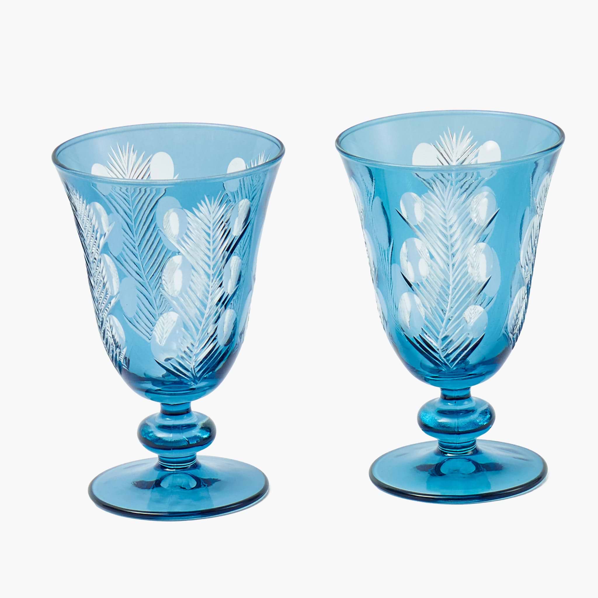 Two blue glass goblets with white floral patterns on a white background