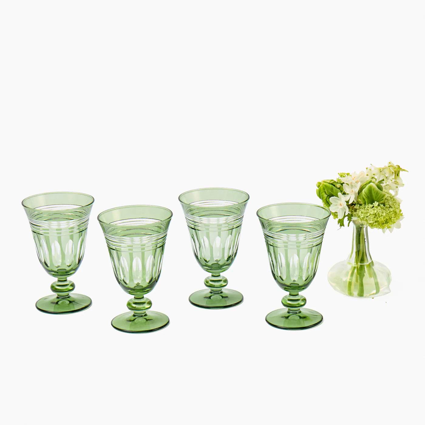 Set of five green glass goblets with a small vase of flowers on a white background