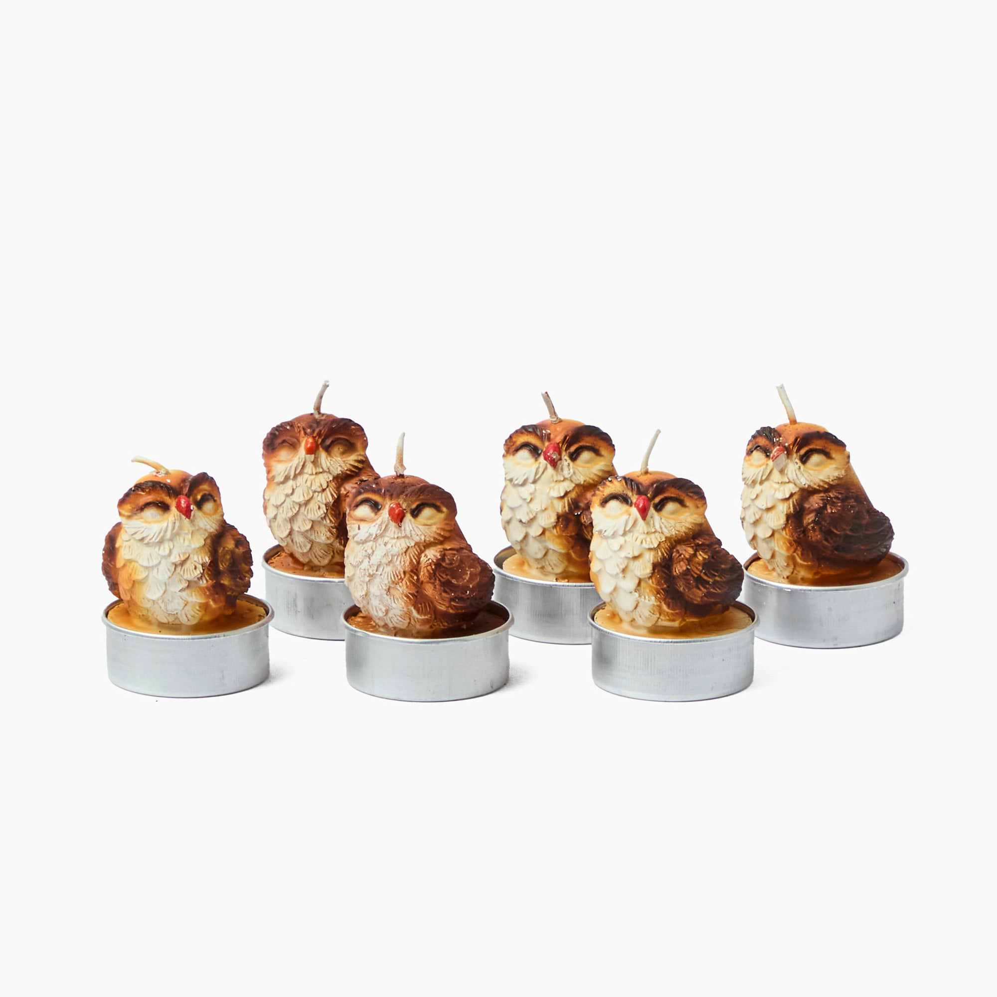 Set of six owl-shaped candles in metal holders on a white background