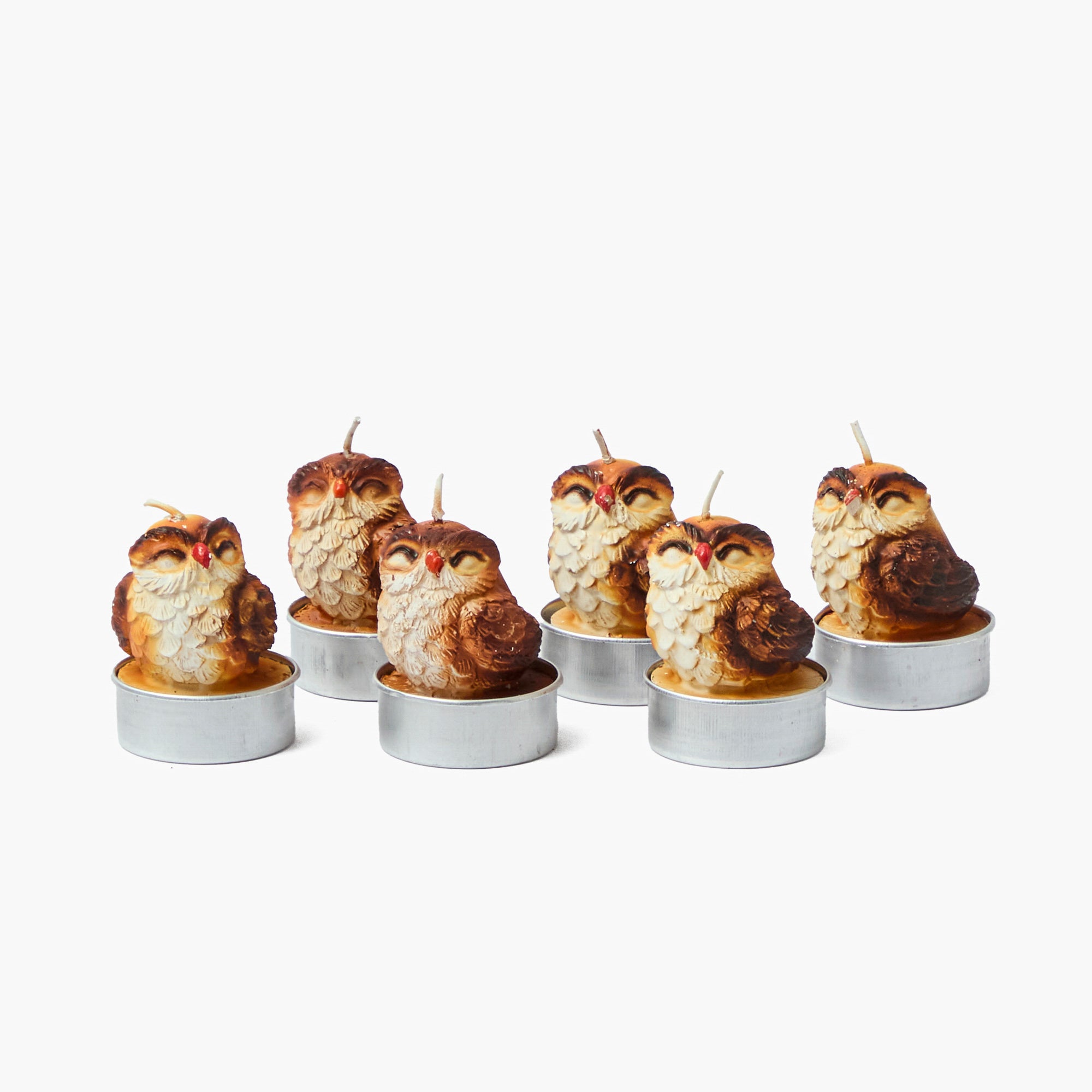 Set of six owl-shaped candles in metal holders on a white background