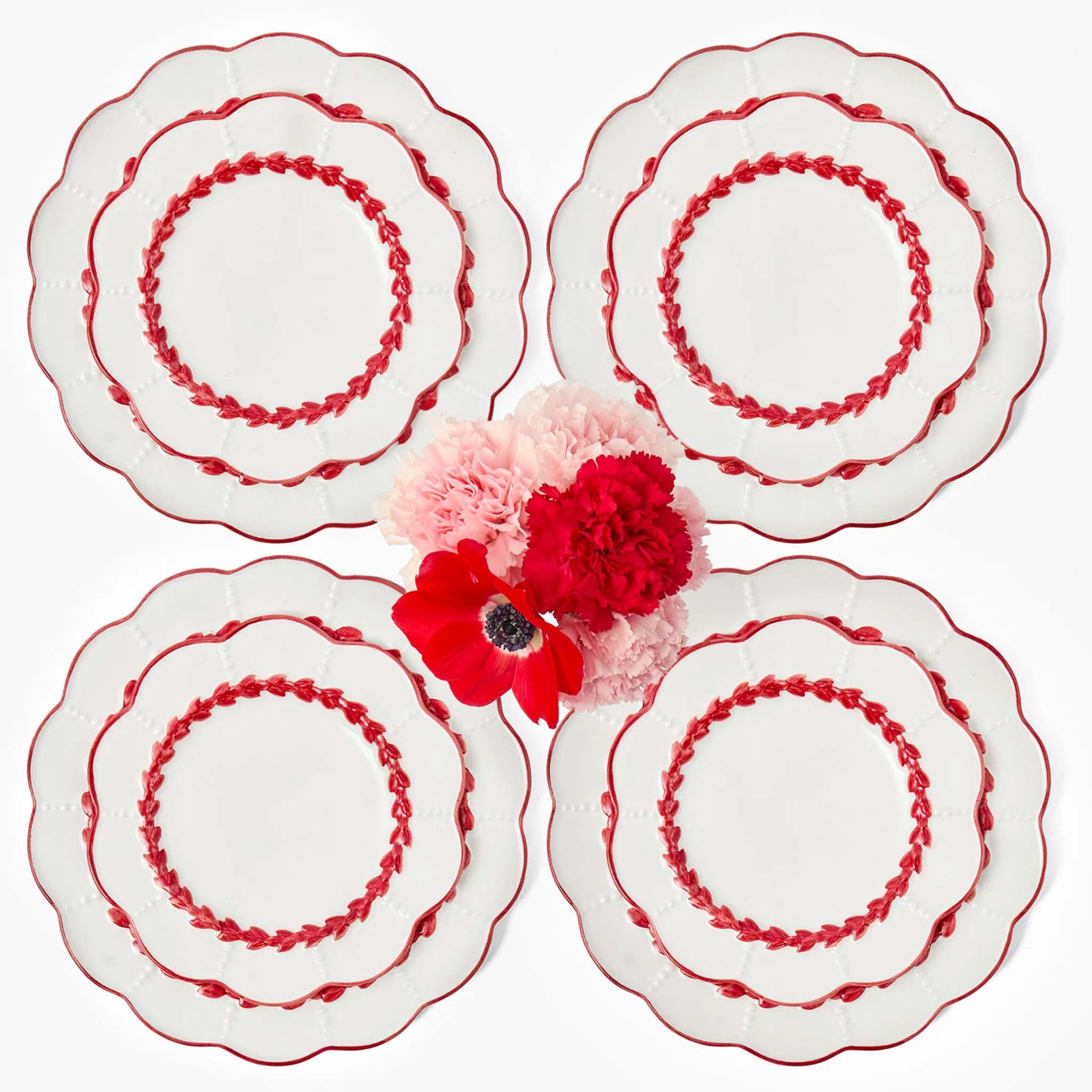Four white plates with red decorative patterns and two decorative flowers on a white background