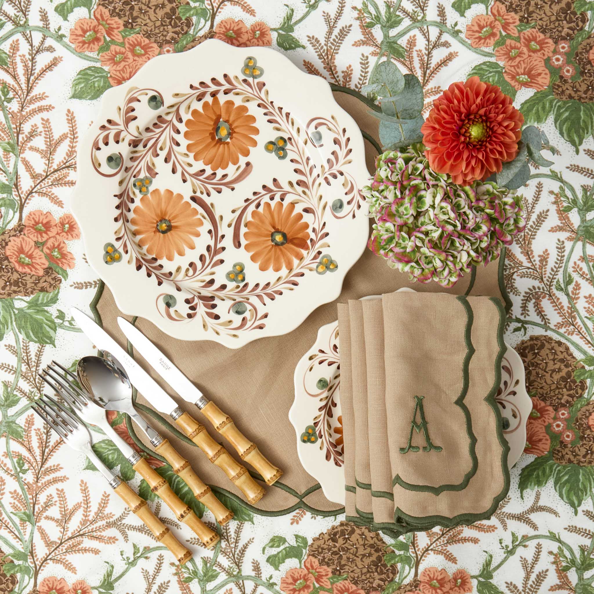 Decorative table setting with floral patterns, plates, bamboo cutlery set, and a napkin on a matching background.