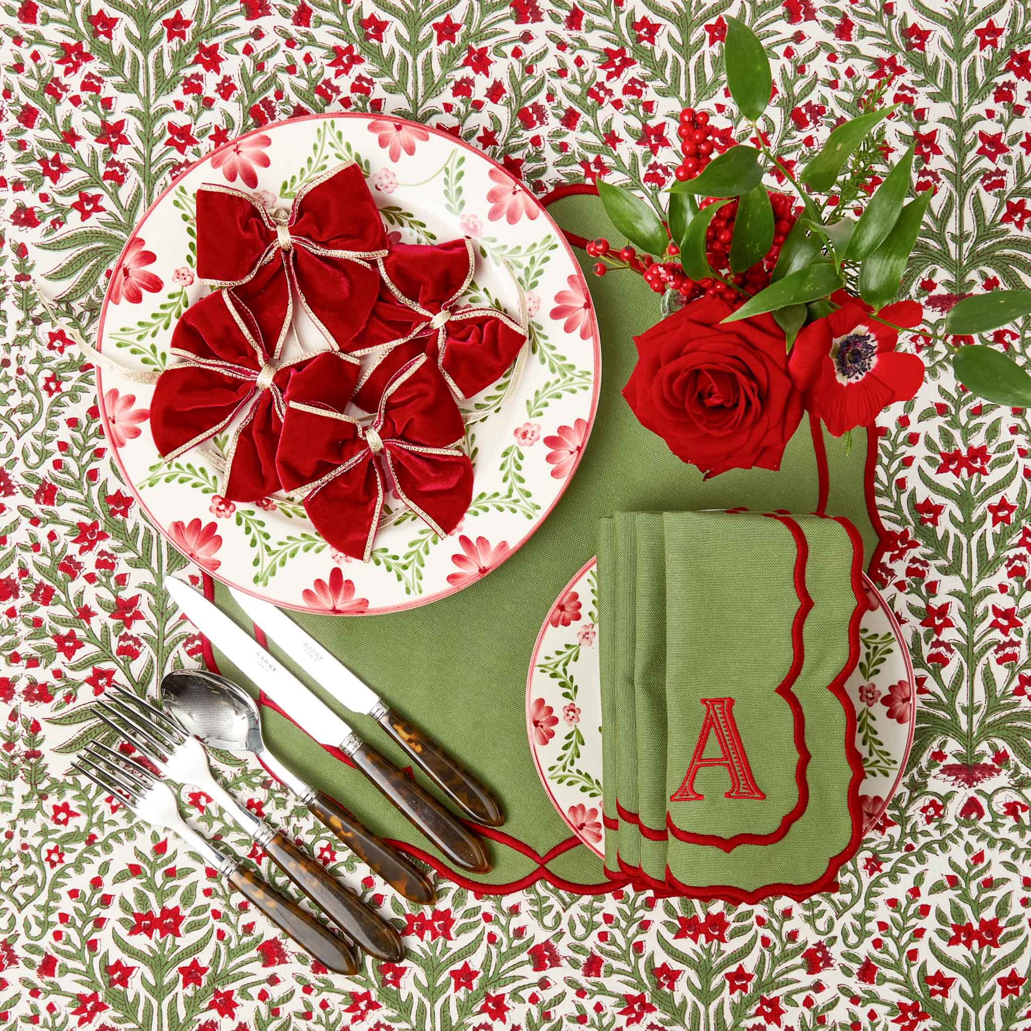 Christmas-themed table setting with red and green decorations, including a plate with red napkins and a floral patterned tablecloth.
