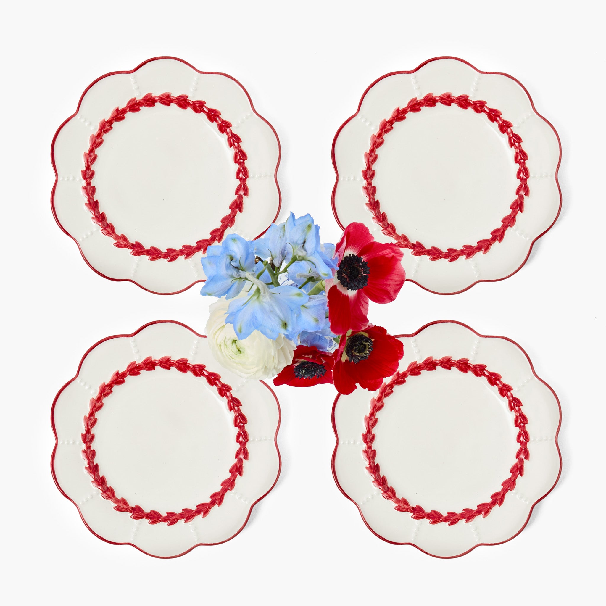 Four white starter plates with red embroidery on a white background, featuring a small arrangement of flowers.