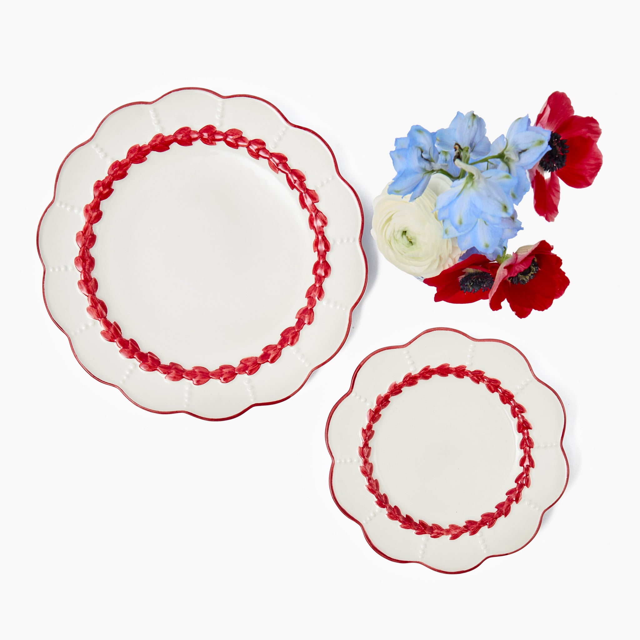 Two decorative plates with red trim and a small arrangement of flowers on a white background