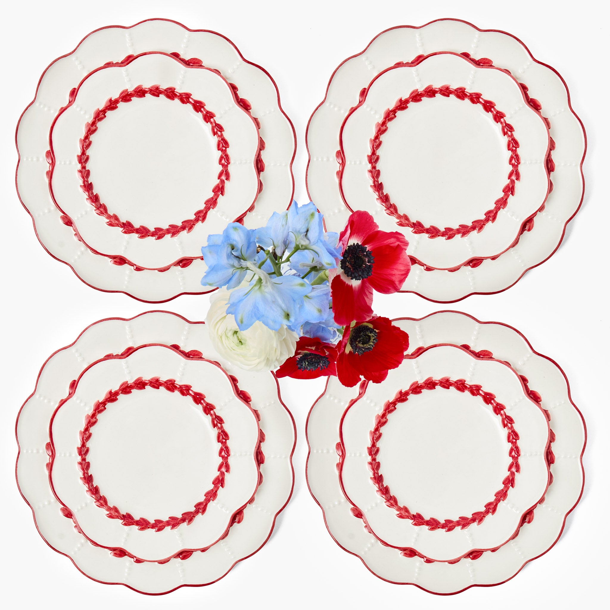 Four white plates with red decorative rim and a small bouquet of flowers in the center on a white background