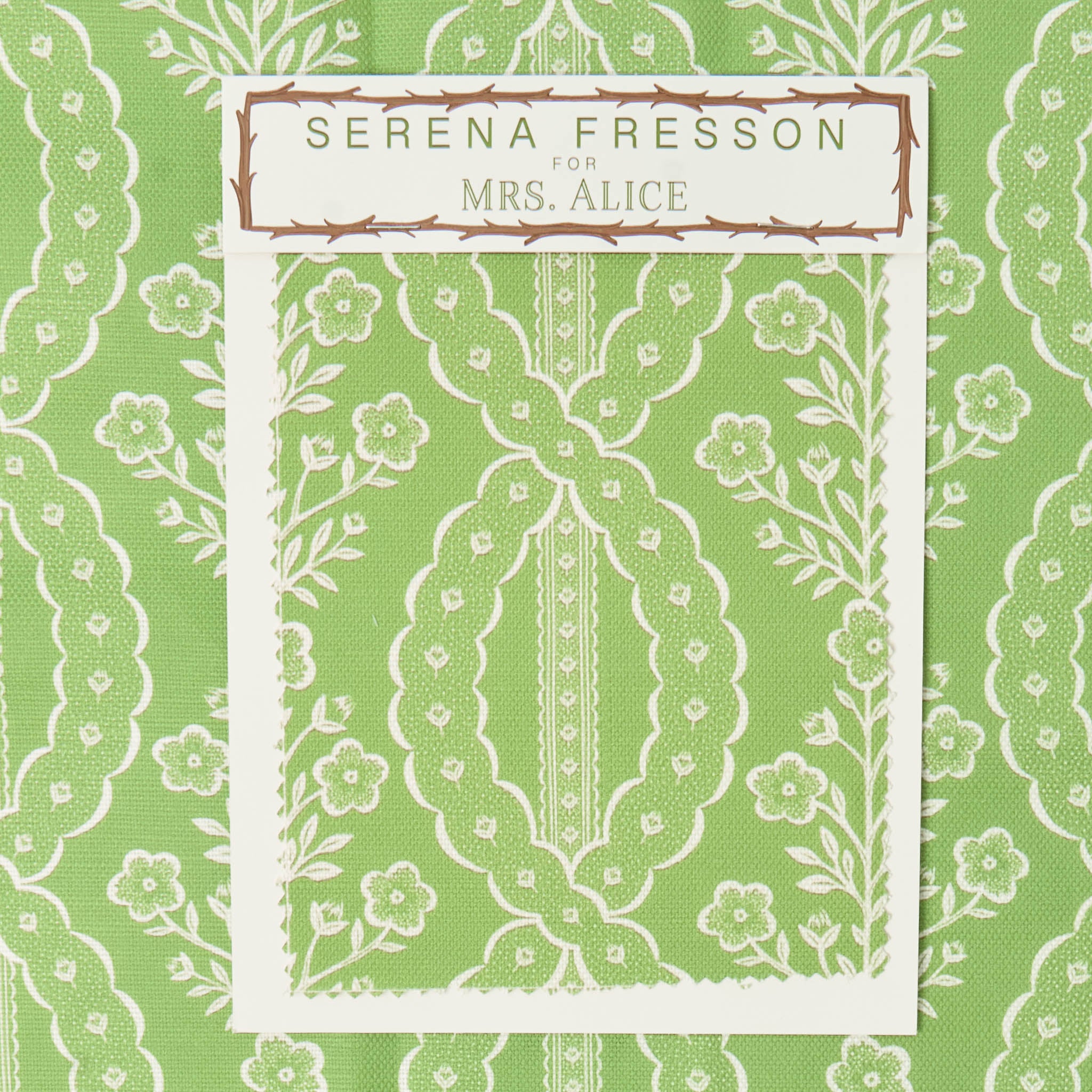 Decorative fabric swatch with floral and leaf pattern on a green background, featuring 'Serena Fresson for Mrs. Alice' label.