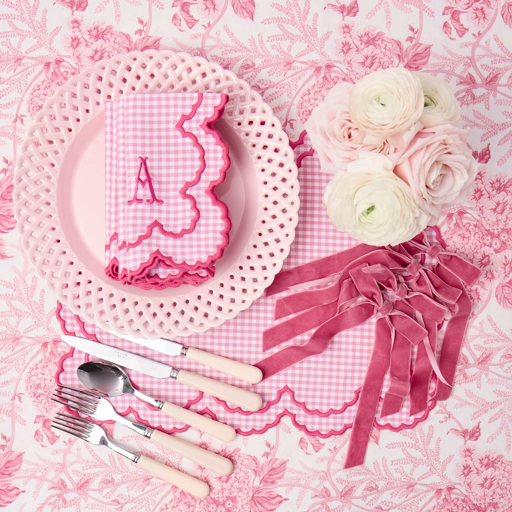 Pink and white place setting with flowers and cutlery on a floral tablecloth