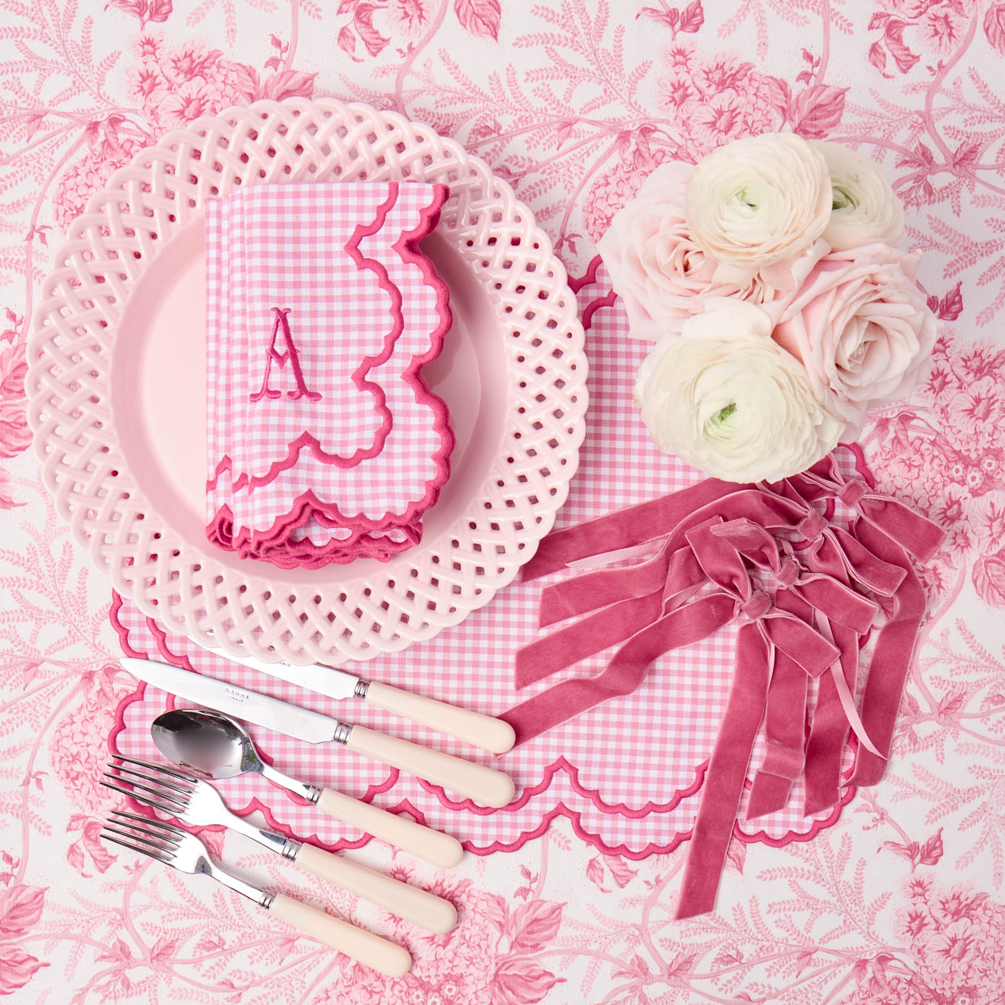 Pink and white place setting with flowers and cutlery on a floral tablecloth