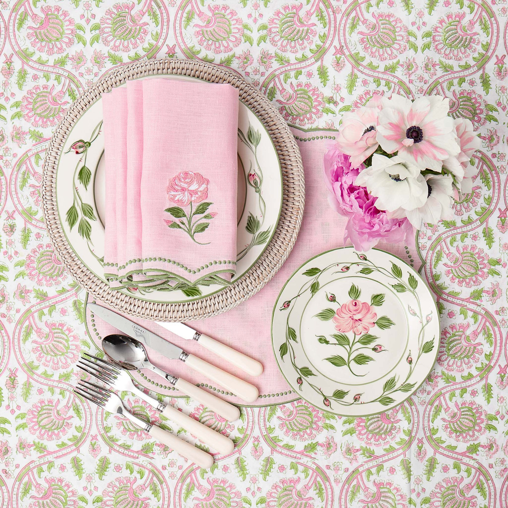 Table setting with floral plates, pink napkin, and flowers on a patterned tablecloth.