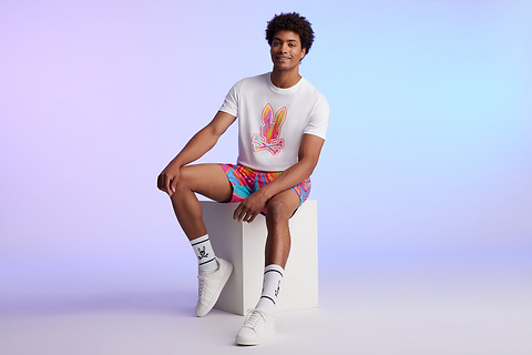 man on a blue background sitting with a white tee with a big bunny and a colorful swim